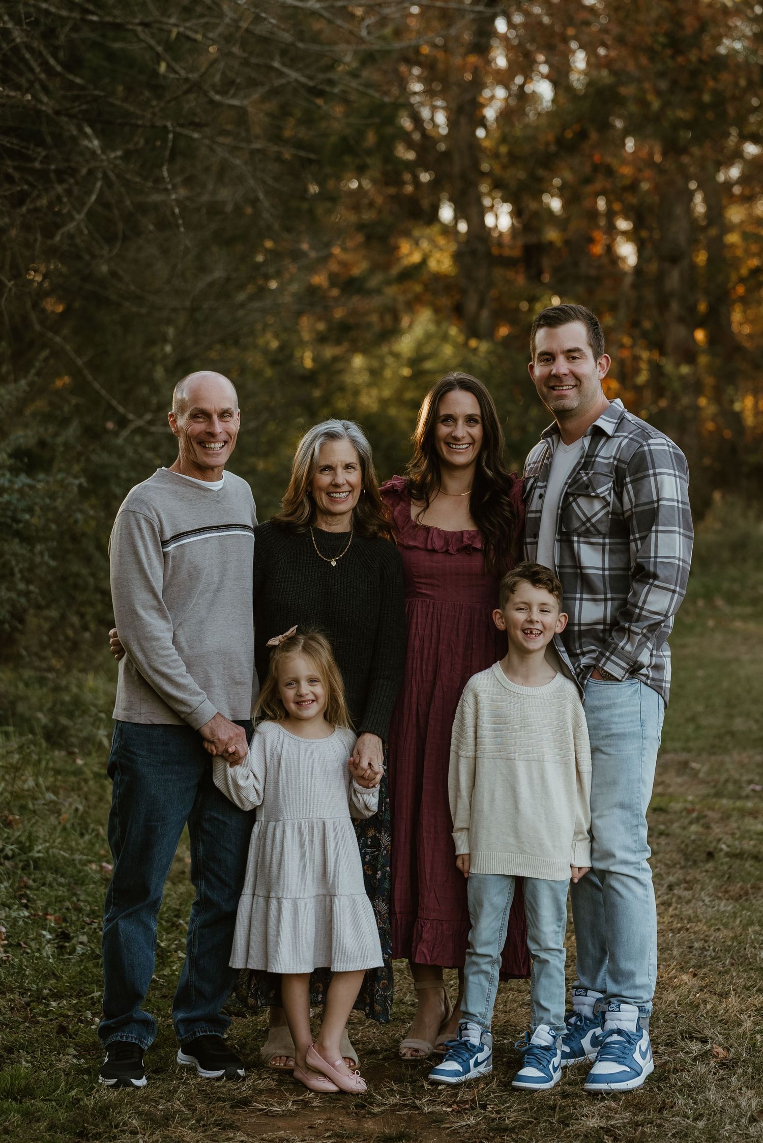 A multigenerational family of six poses together smiling in a colorful autumn forest setting.