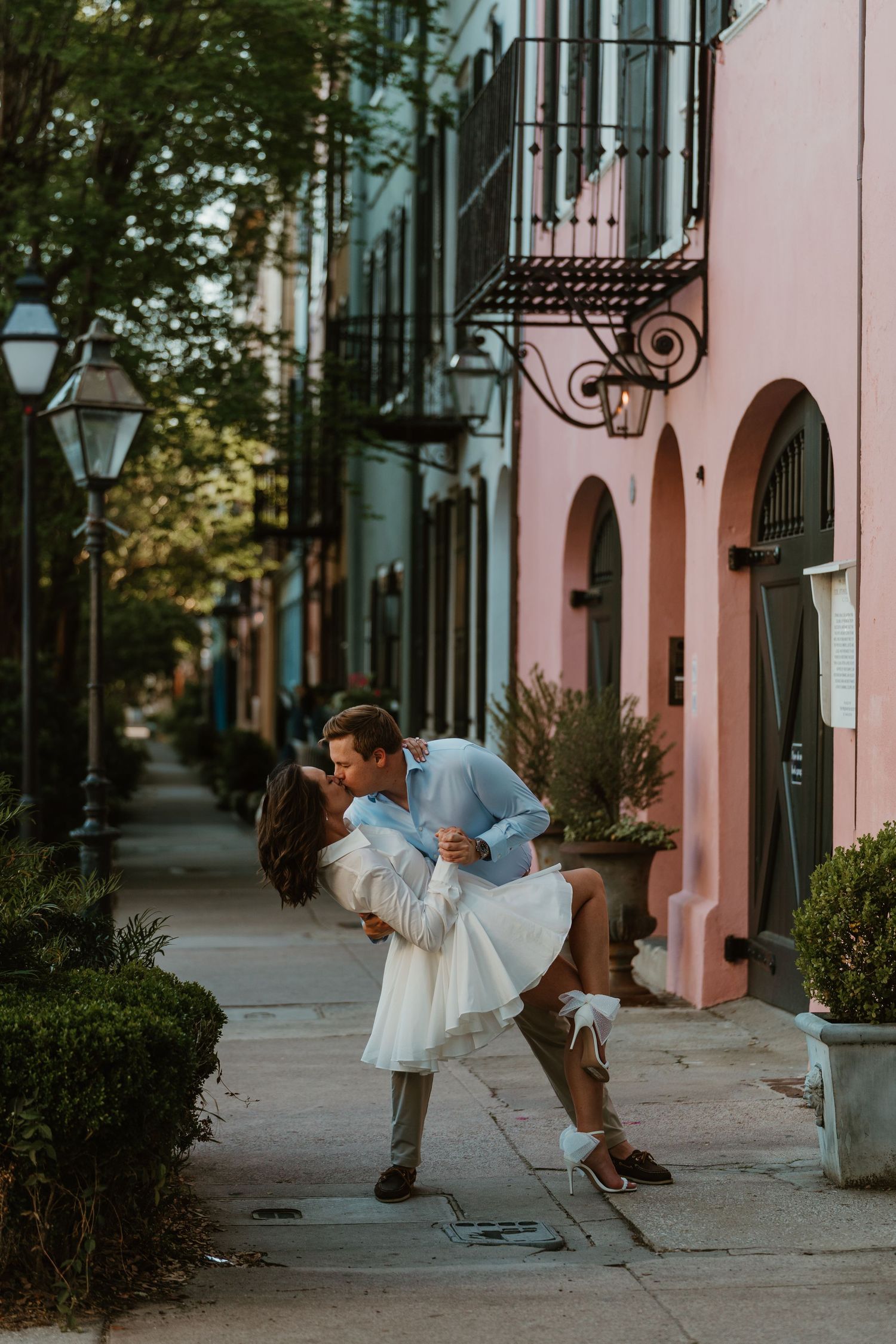 Couple sharing a romantic dip kiss on a colorful Charleston Rainbow Row sidewalk during golden hour.