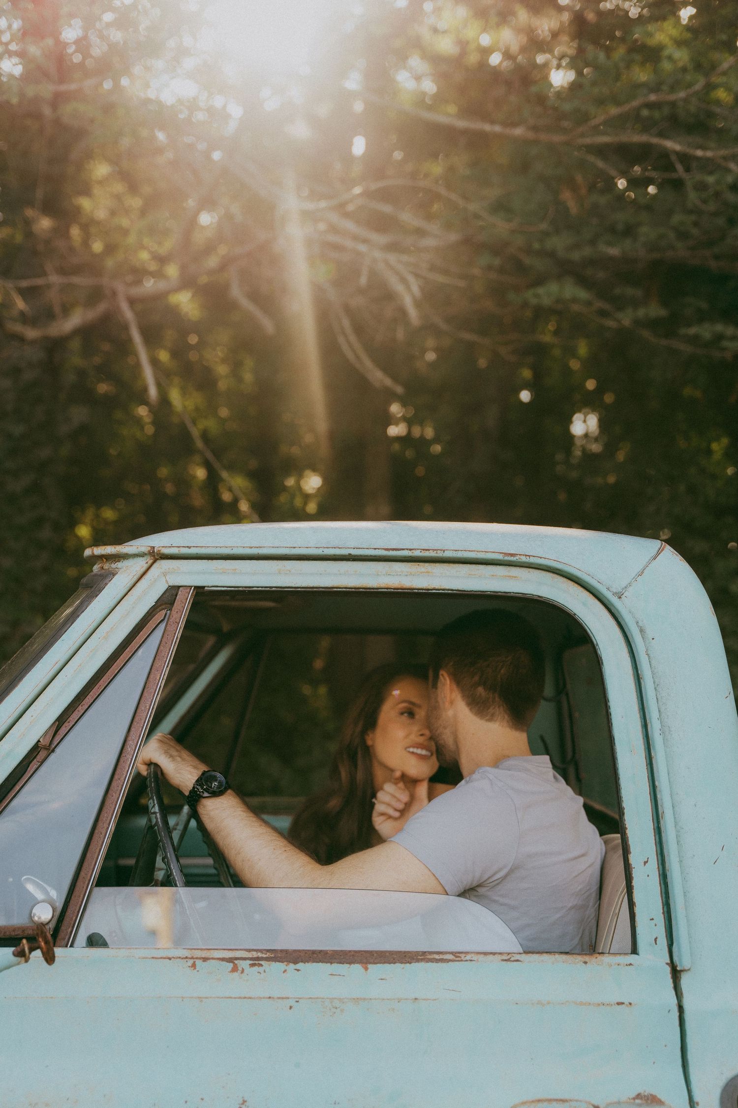 Couple sharing a tender moment inside a vintage light blue pickup truck at sunset.