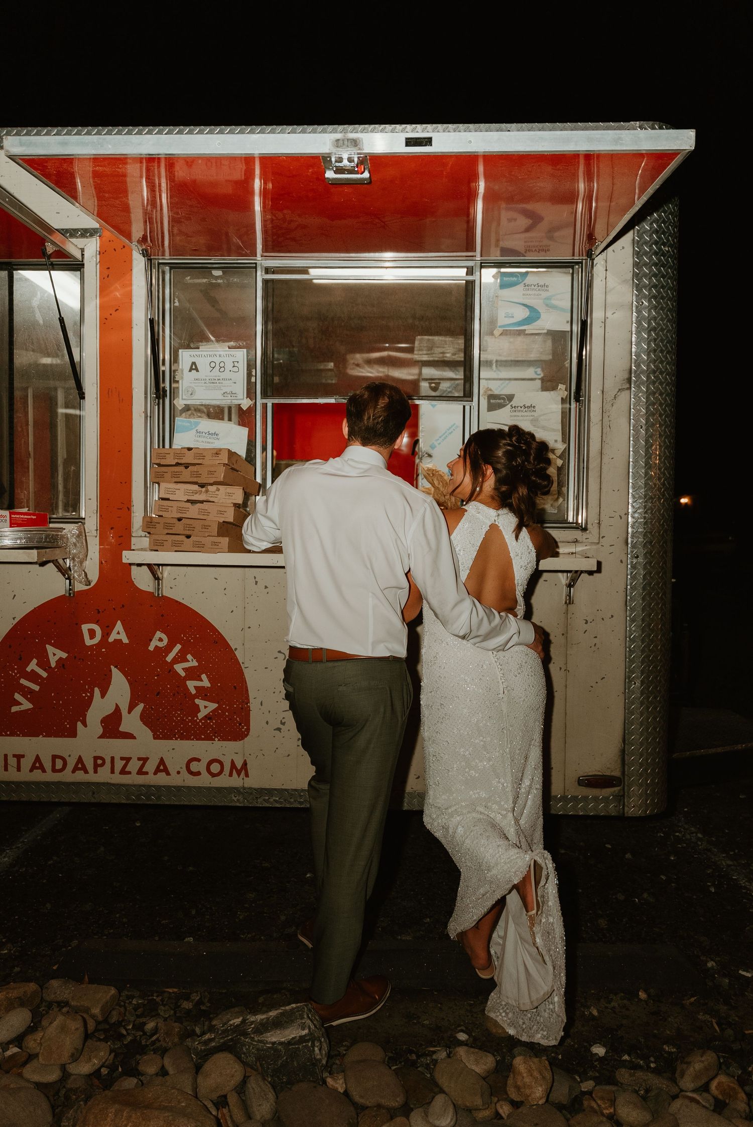 Newlywed couple ordering late night pizza from Vita Da Pizza food truck at wedding reception.