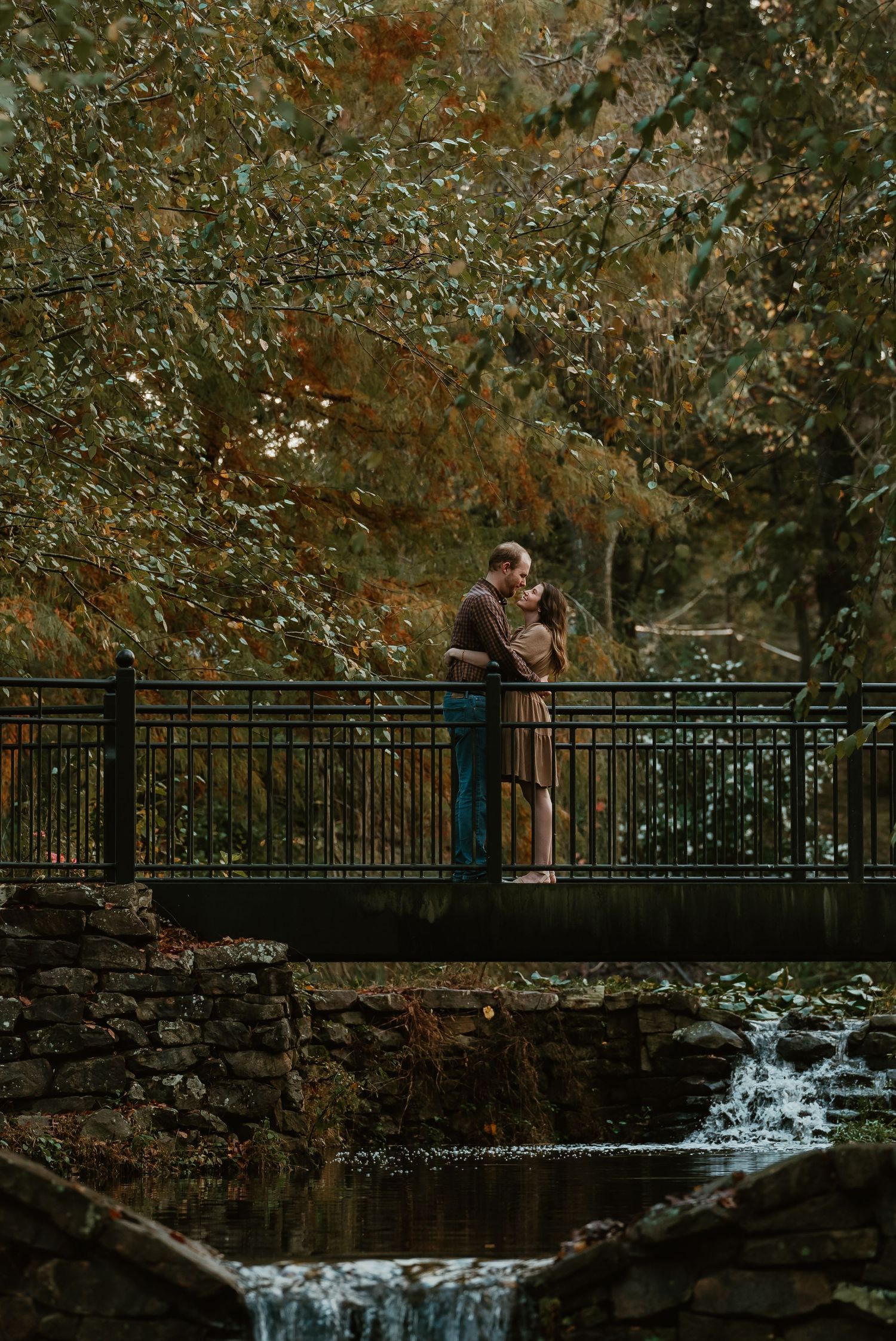 Couple kissing on a stone bridge over a waterfall in an autumn forest.