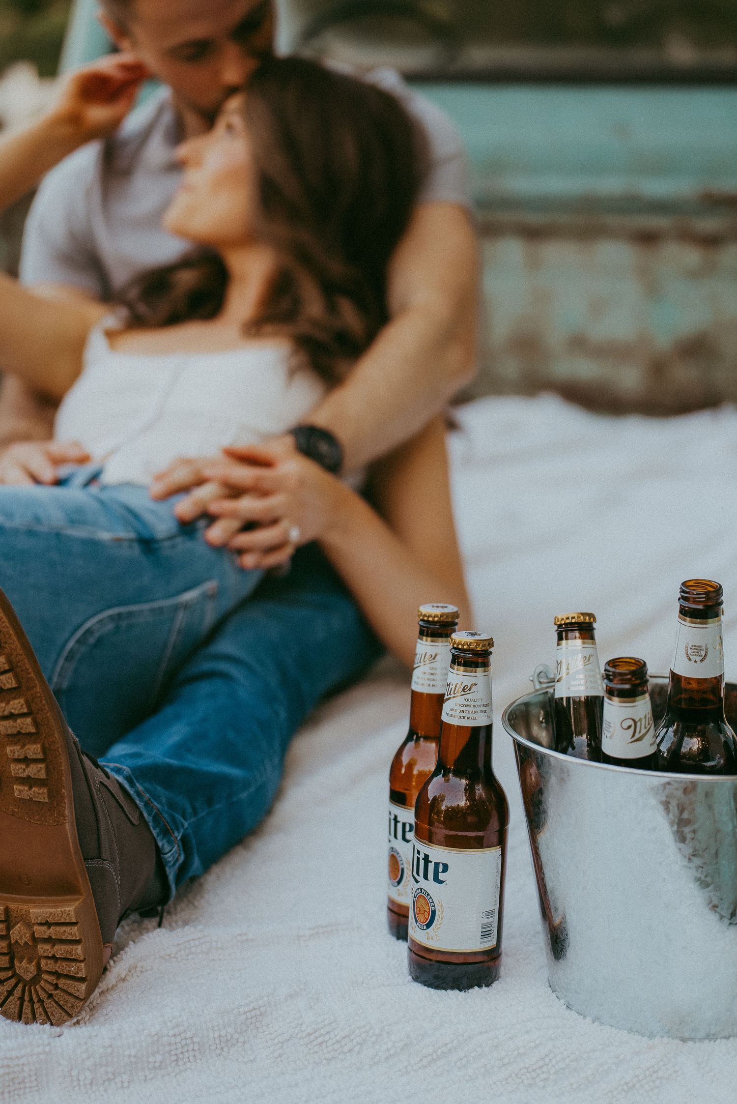 Couple relaxing on a blanket with Miller Lite beer bottles in a bucket during outdoor photo session.
