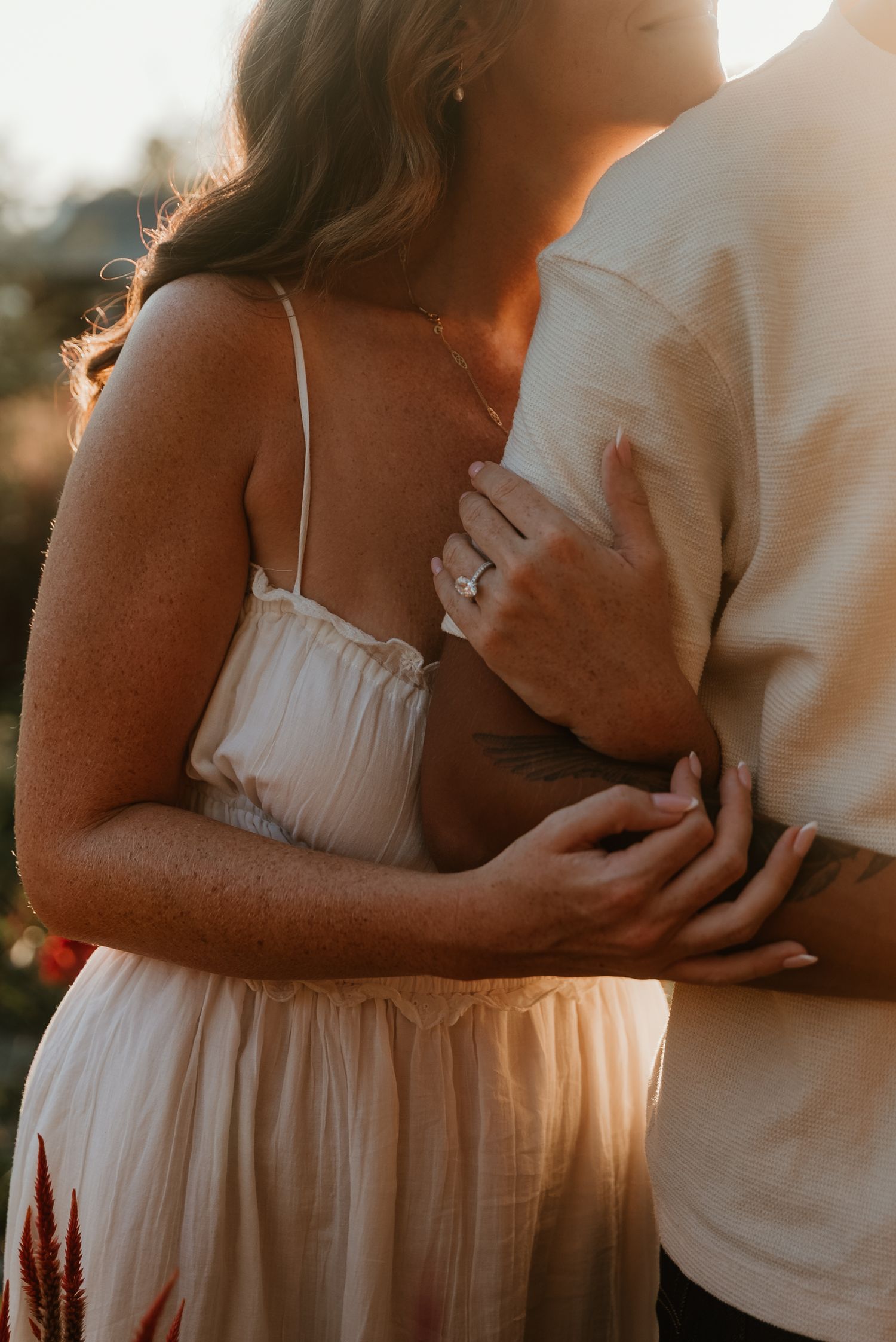 Close-up of engaged couple embracing, showcasing diamond engagement ring in warm sunset light.