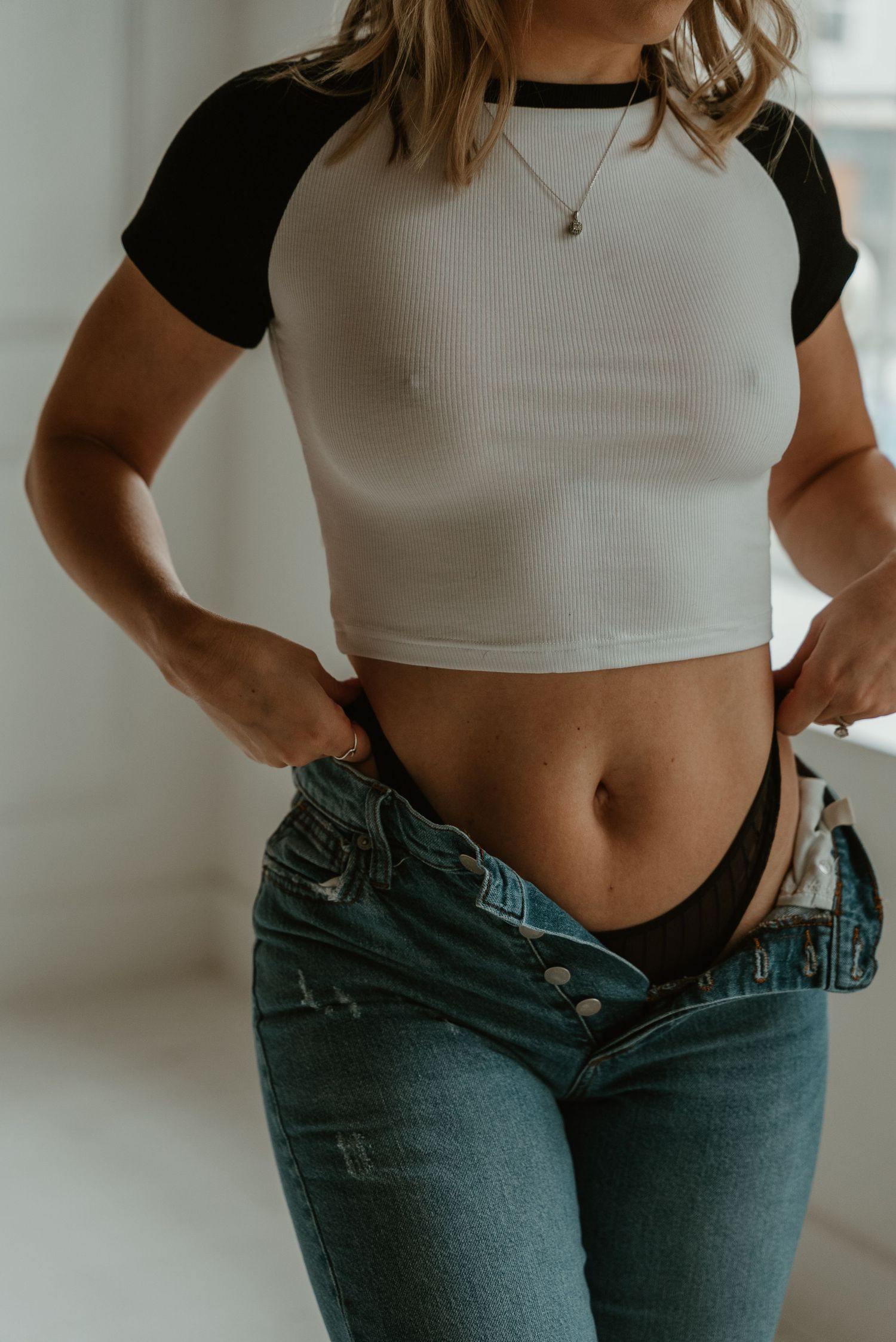 Woman in white crop top pulling down jeans to reveal black underwear.