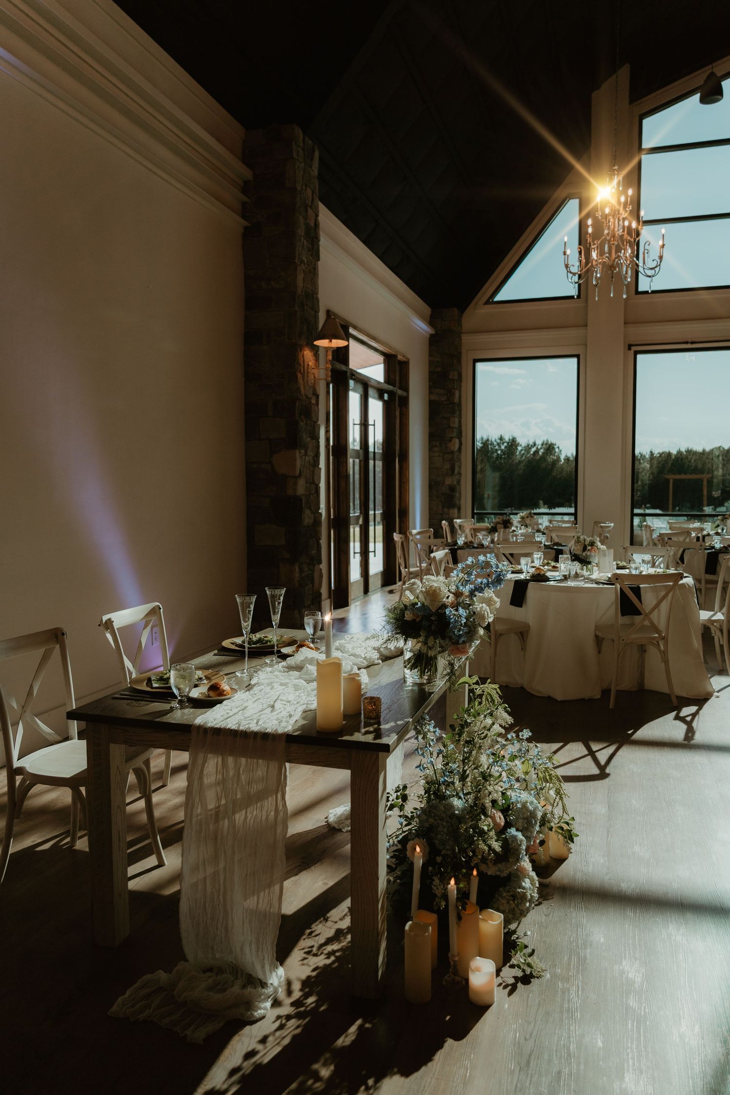 Elegant wedding reception hall with long decorated tables, candles, floral arrangements and chandelier.