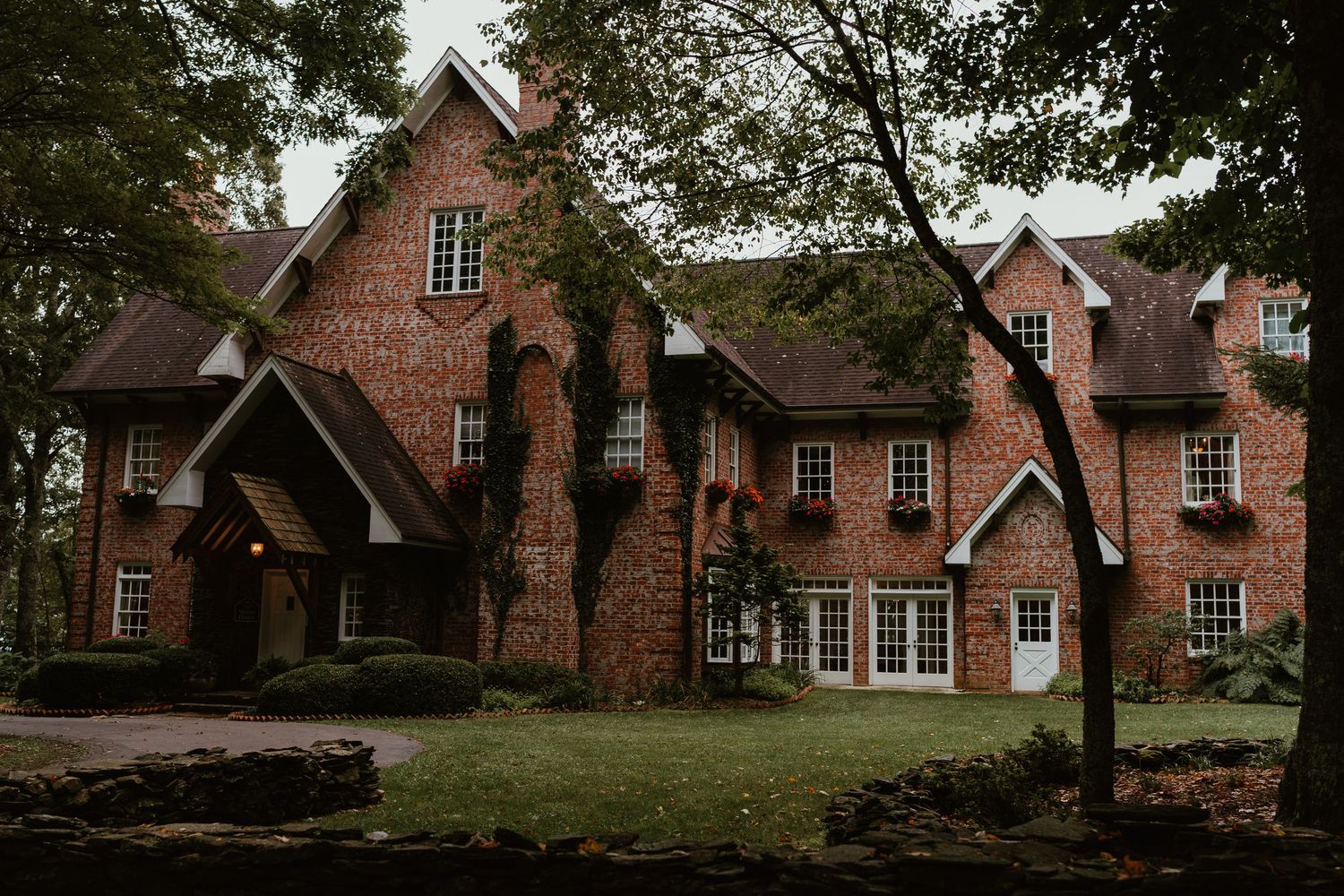 Elegant red brick Tudor-style mansion surrounded by lush green trees and manicured lawn.