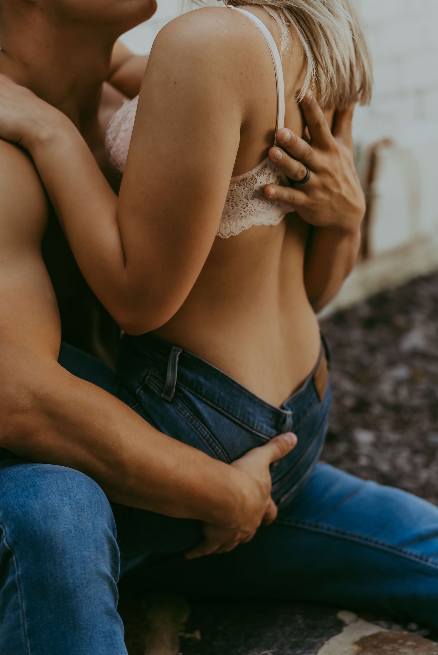 Close-up of a couple in an intimate embrace, woman wearing a lace bra and jeans, man holding her close.