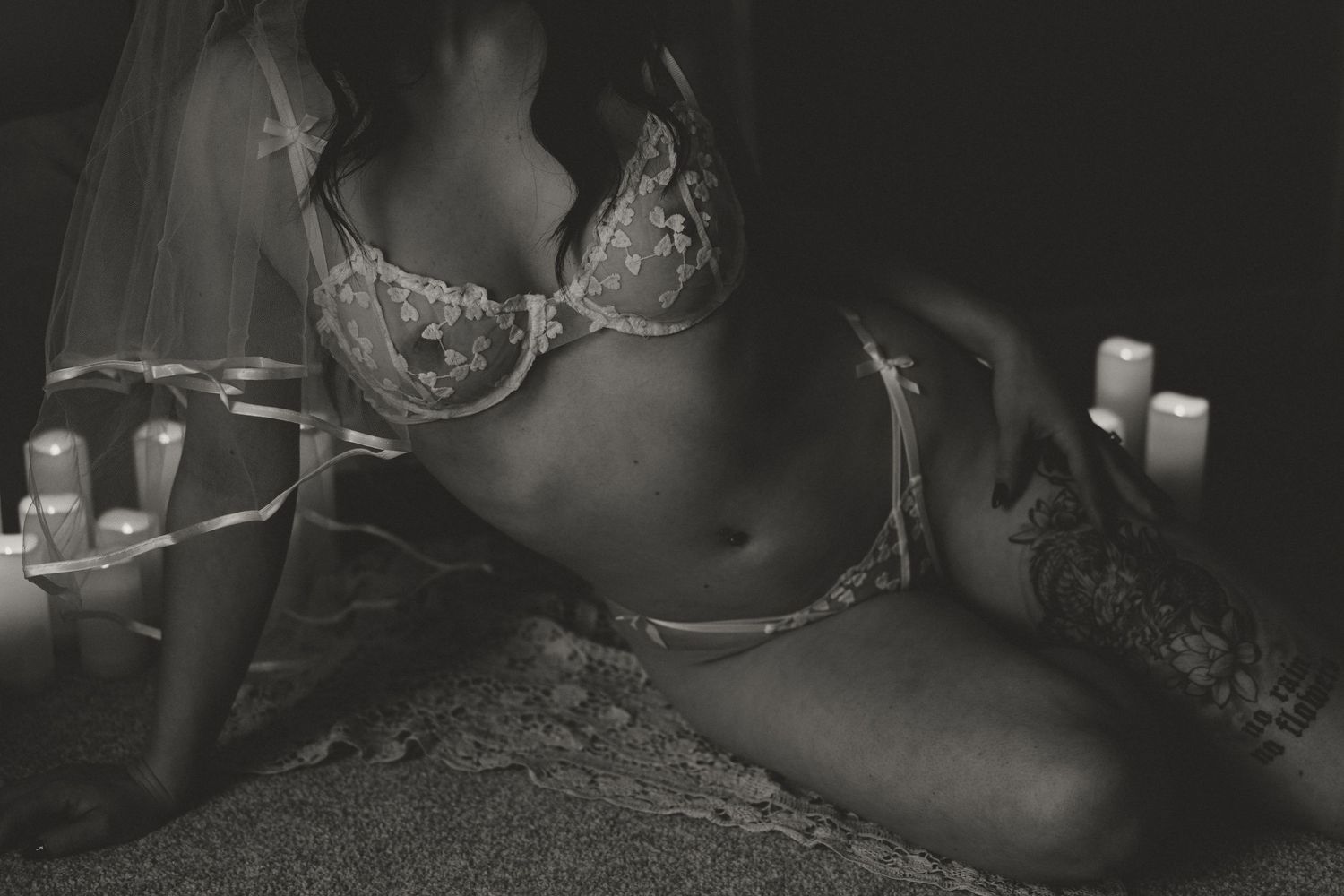 Black and white photo of a woman in lace lingerie lying on sand surrounded by candles with veil.