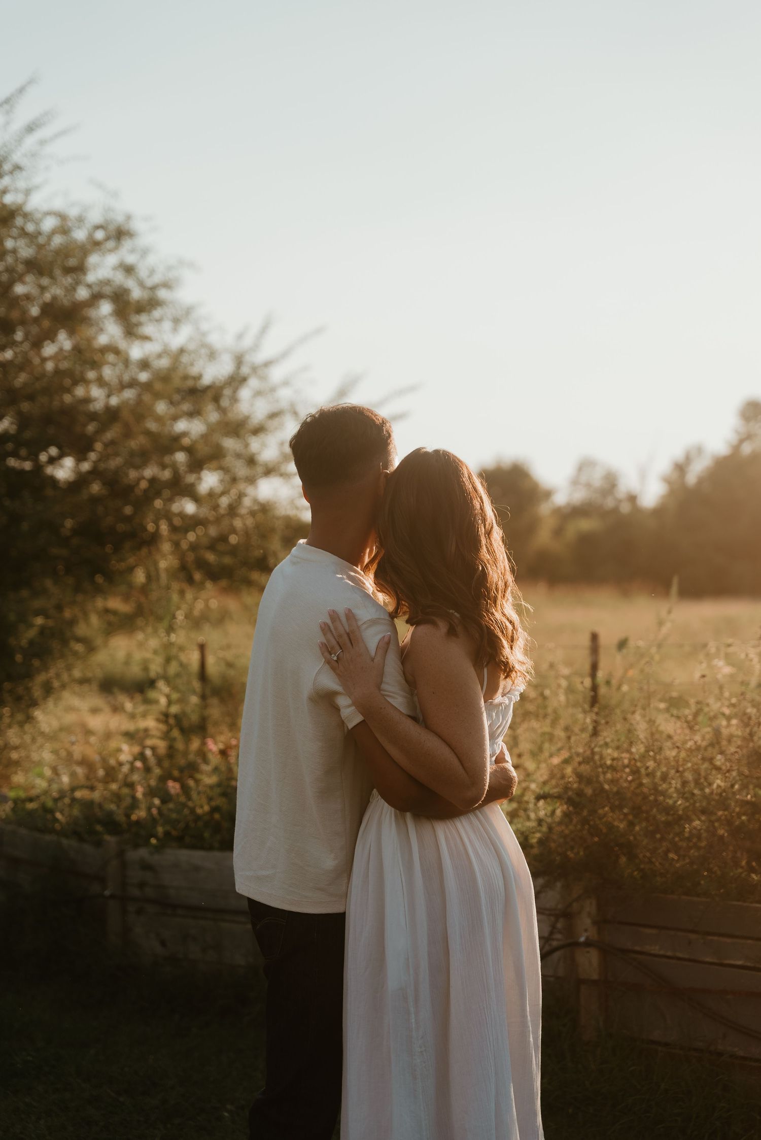Couple embracing closely in a wildflower meadow during warm glowing golden hour sunset.