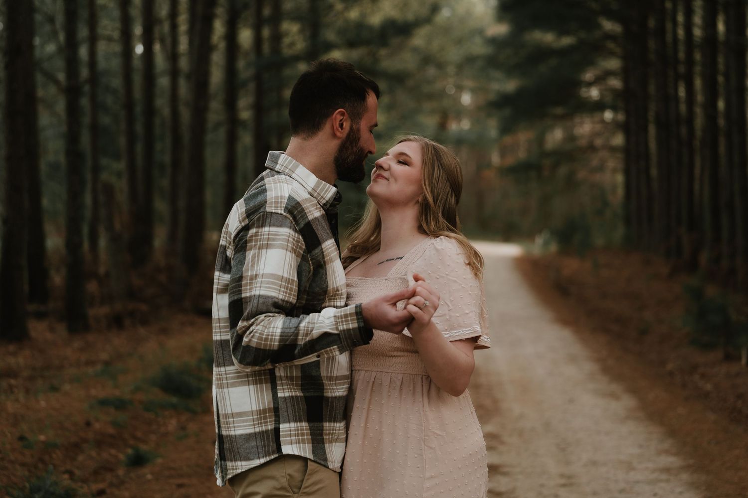 Couple holding hands and smiling at each other on a wooded forest trail.