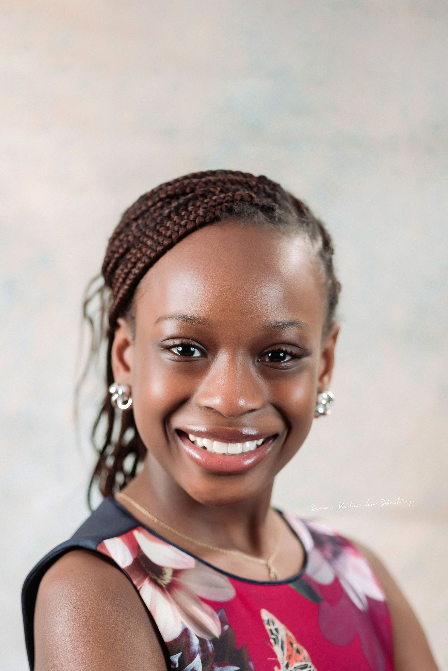 Beauty portrait showing elegant braided hairstyle and floral dress against neutral background.