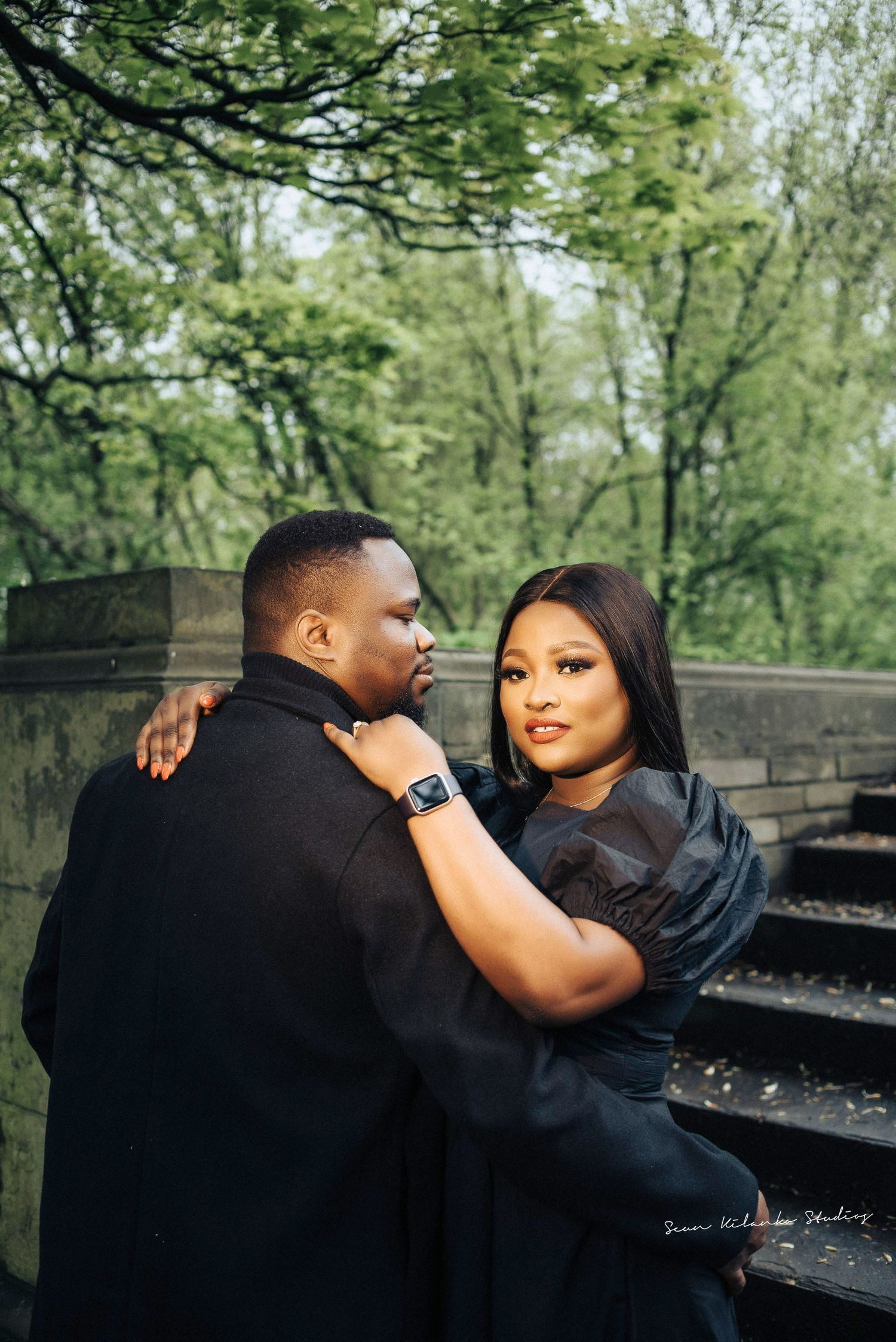 Couple embraces while standing on historic stone steps with green foliage in the background.