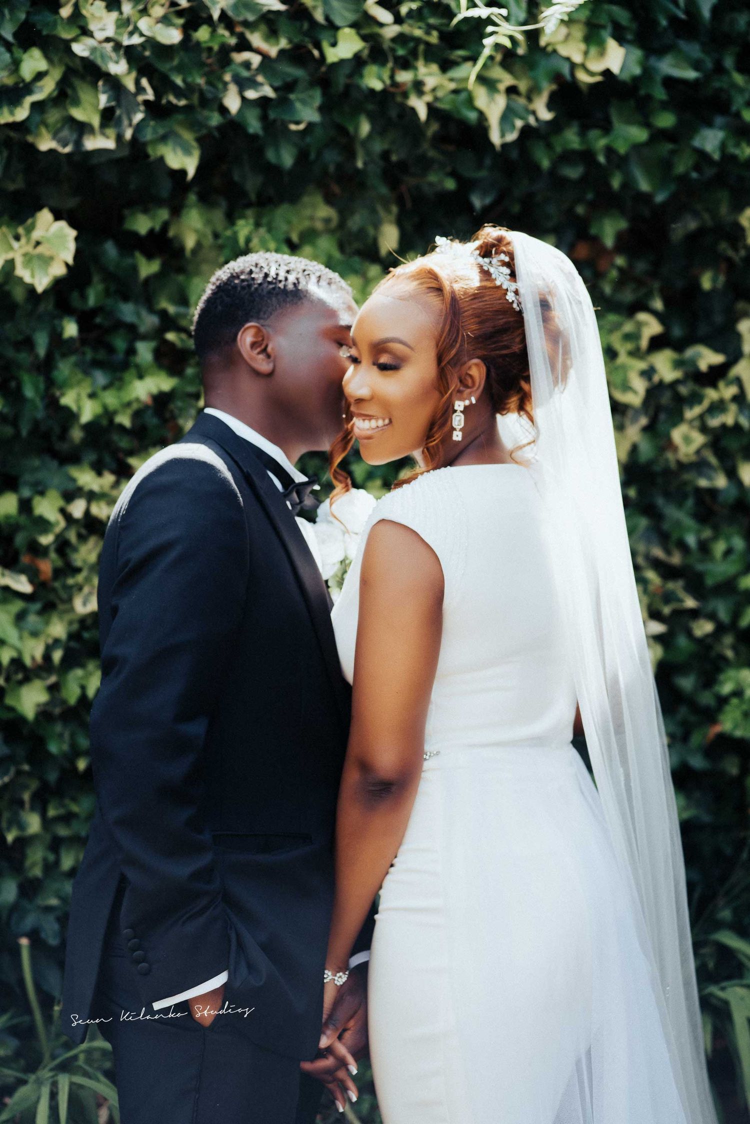 Candid wedding photo of newlyweds sharing a joyful moment against a leafy backdrop.