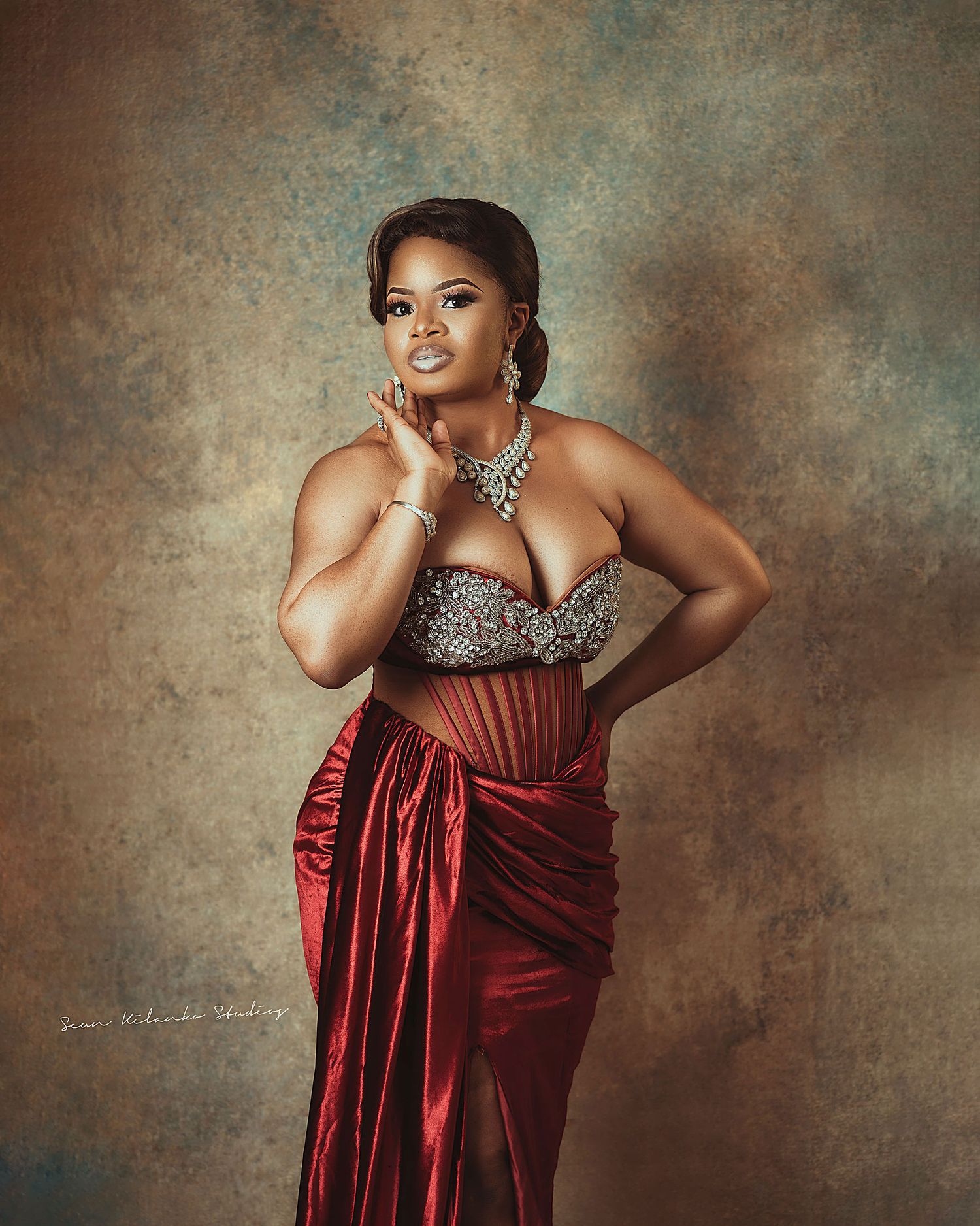 Elegant portrait featuring a woman in a red silk gown and silver jewelry against a mottled background.