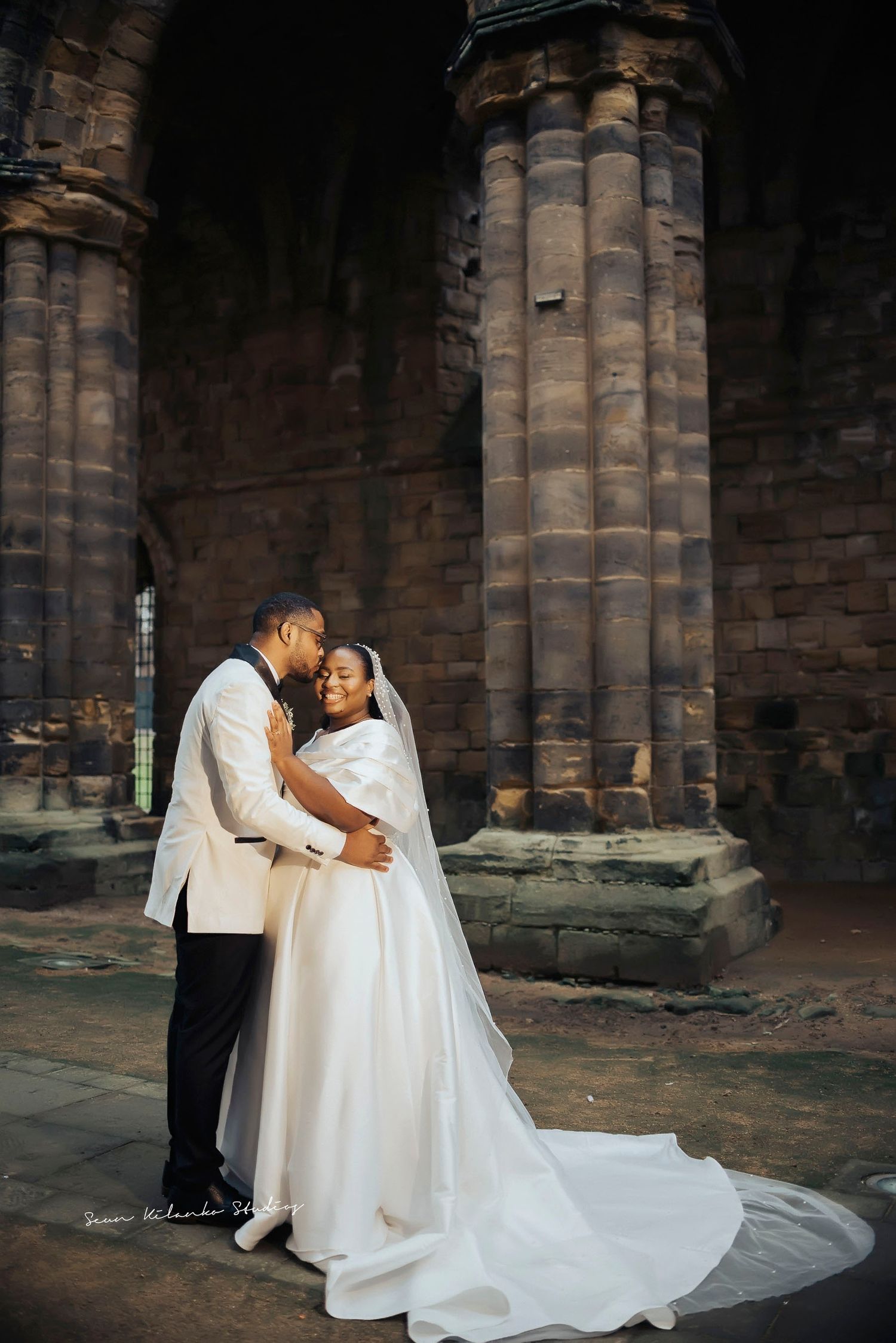 A romantic wedding moment captured beneath towering stone pillars of a historic church.