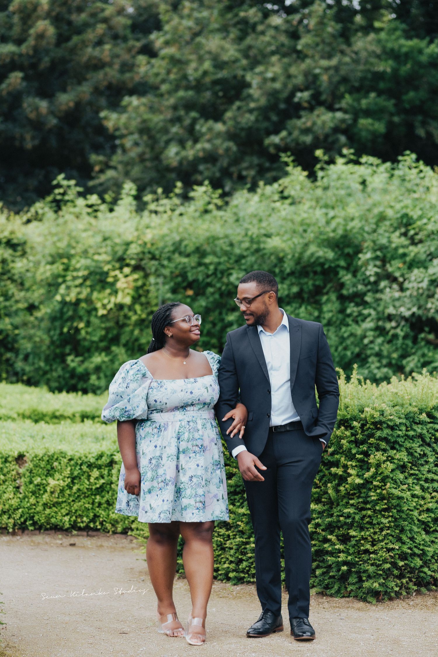 Couple strolls together on garden path wearing coordinated formal outfits.