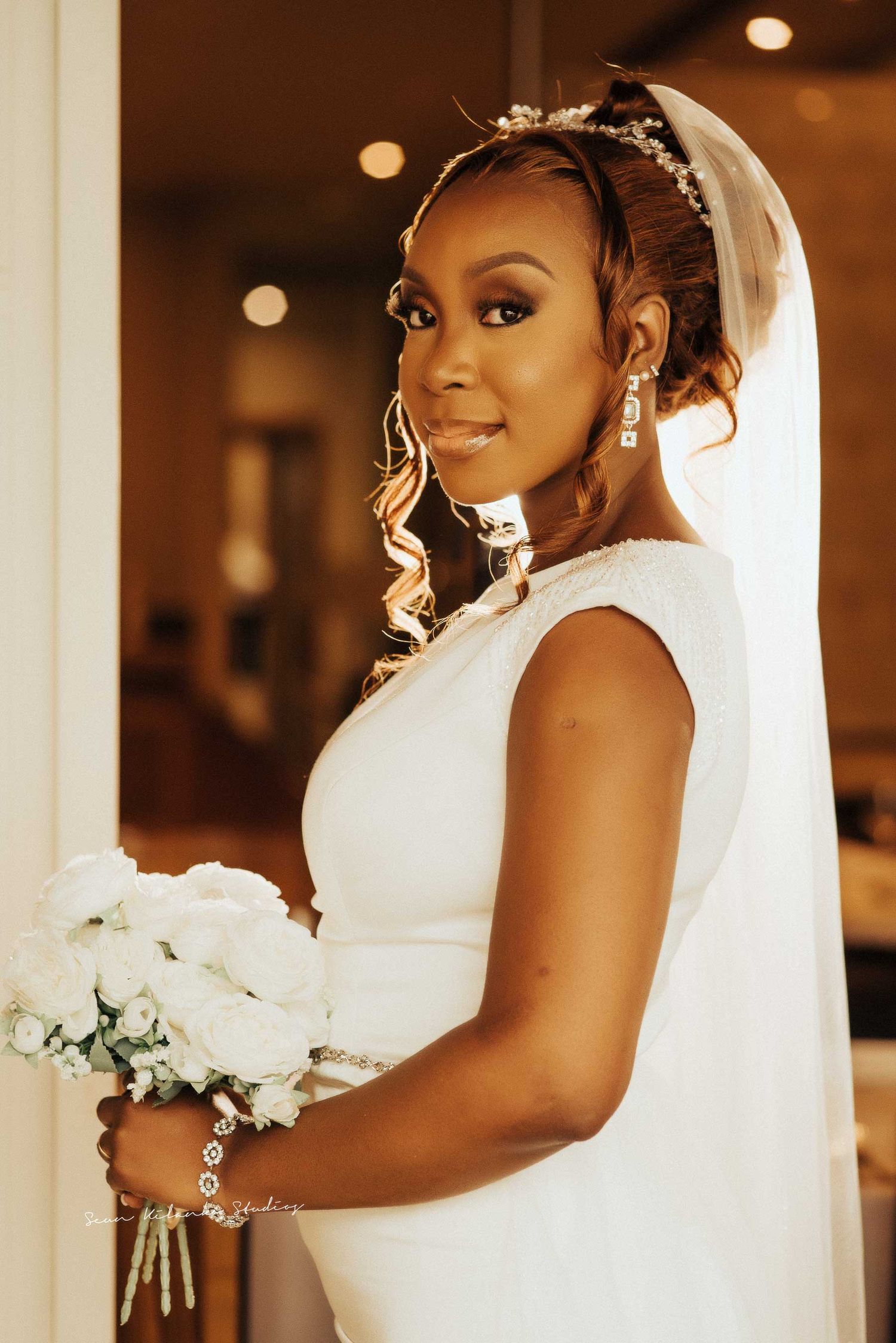 A radiant bride holding white flowers poses in an elegant sleeveless wedding dress and veil.