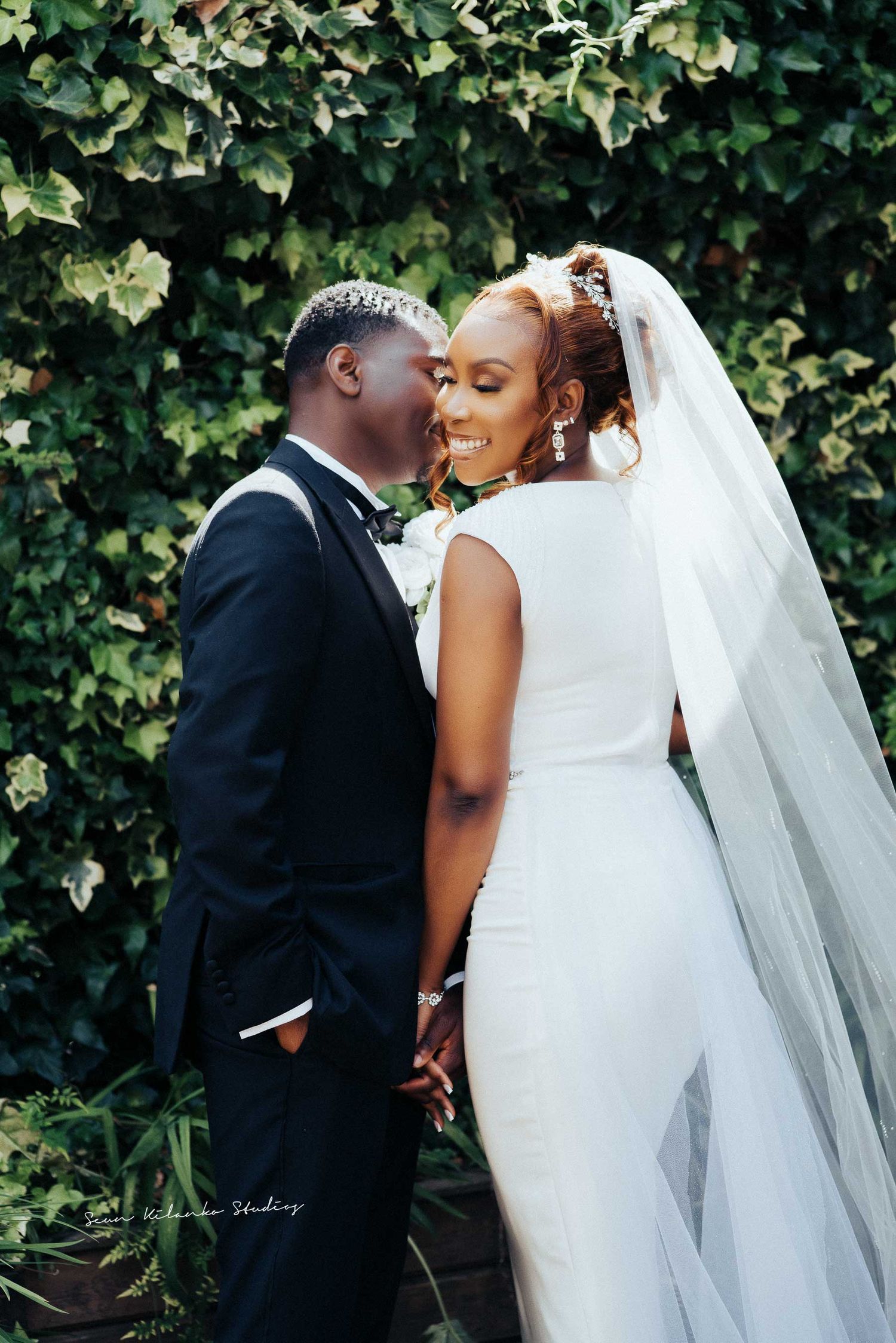A tender wedding moment captured as newlyweds share an intimate moment against green foliage.