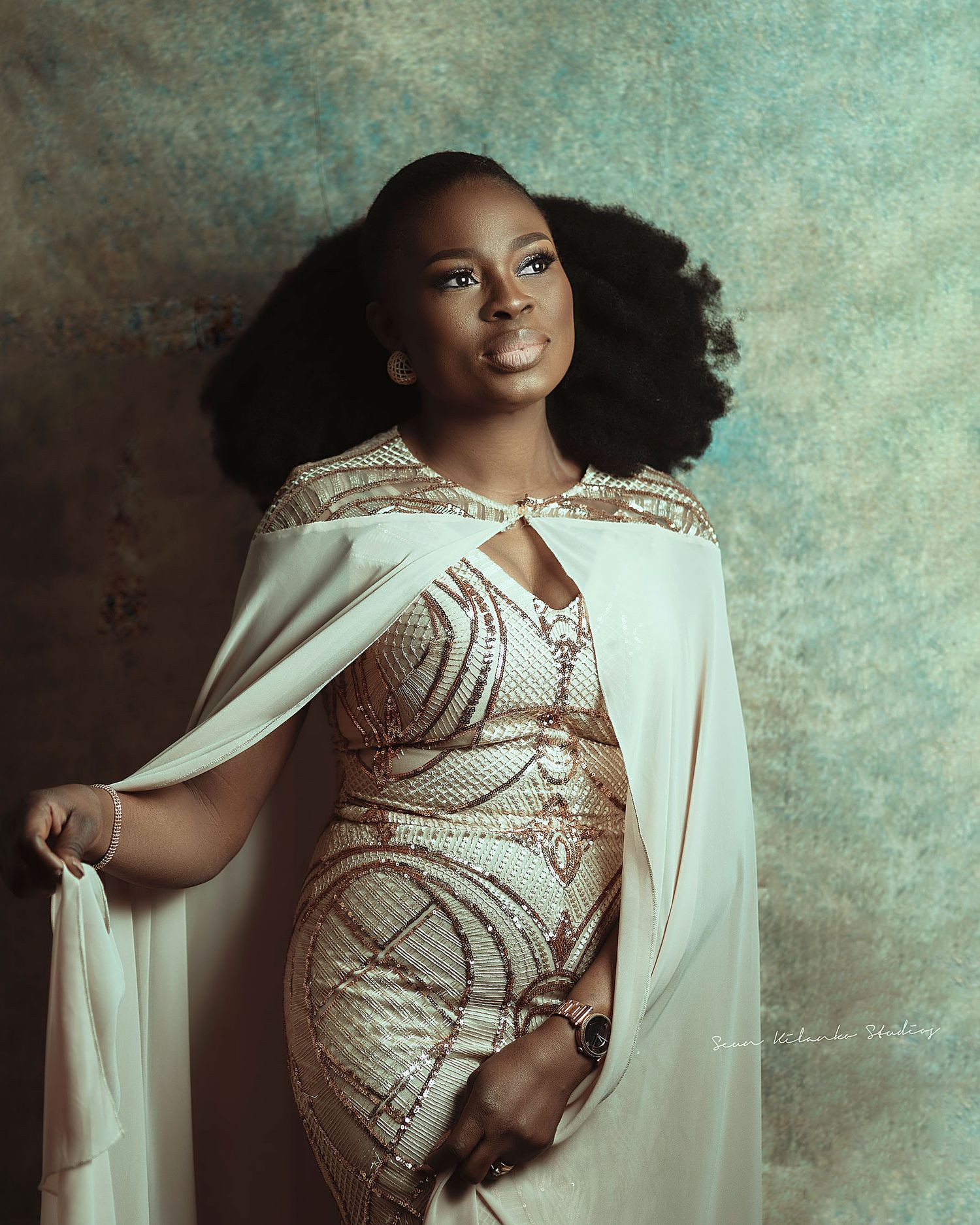 Fashion portrait in fitted beige beaded dress with dramatic cape detail.