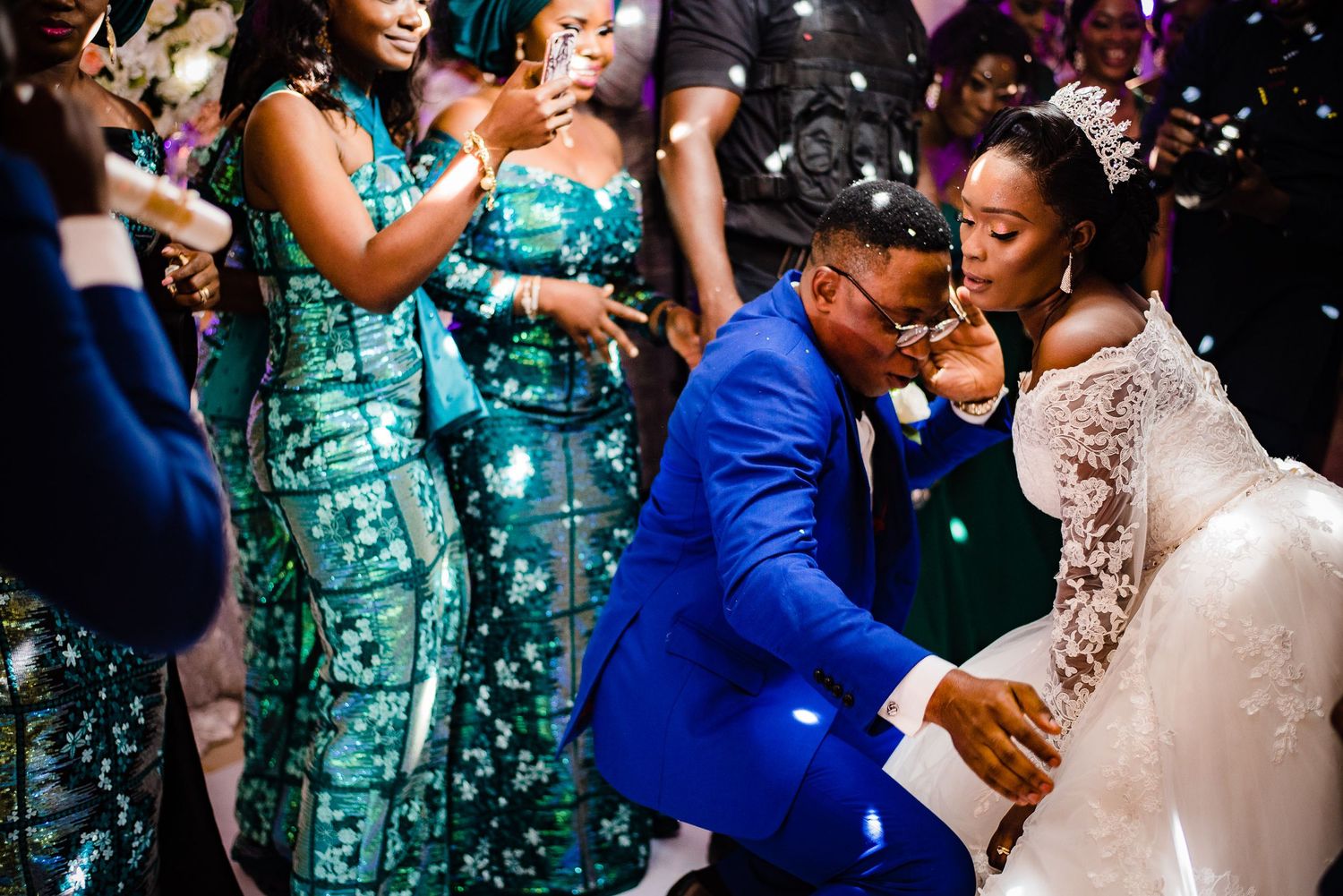 A couple celebrates on the dance floor at their wedding reception while bridesmaids in matching green dresses watch nearby.
