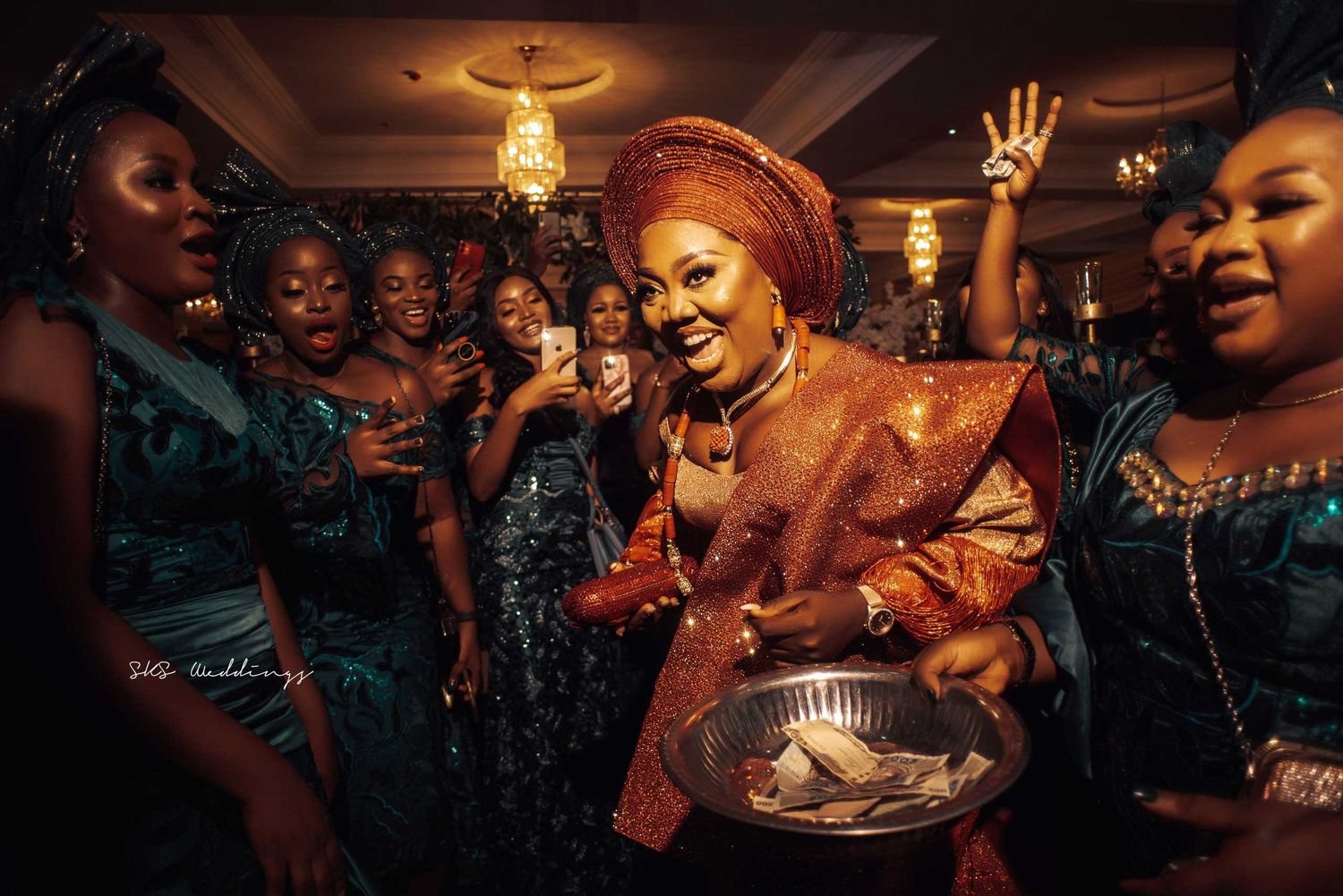 Vibrant wedding celebration with dancers in traditional attire dancing and celebrating at an ornately decorated indoor venue.