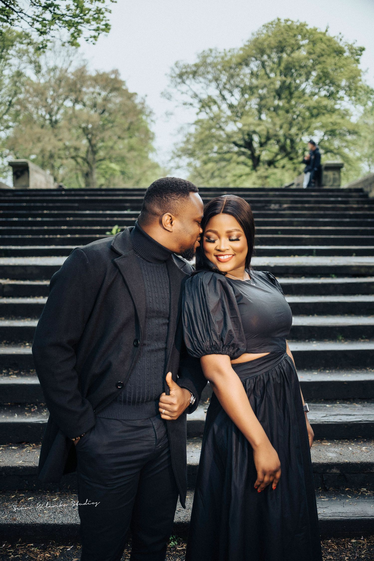 Affectionate couple in black attire shares a tender moment on grand outdoor steps.