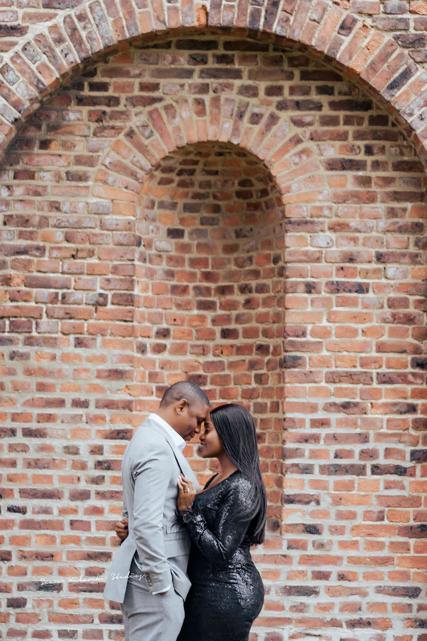 Intimate couple moment against rustic brick archway backdrop.