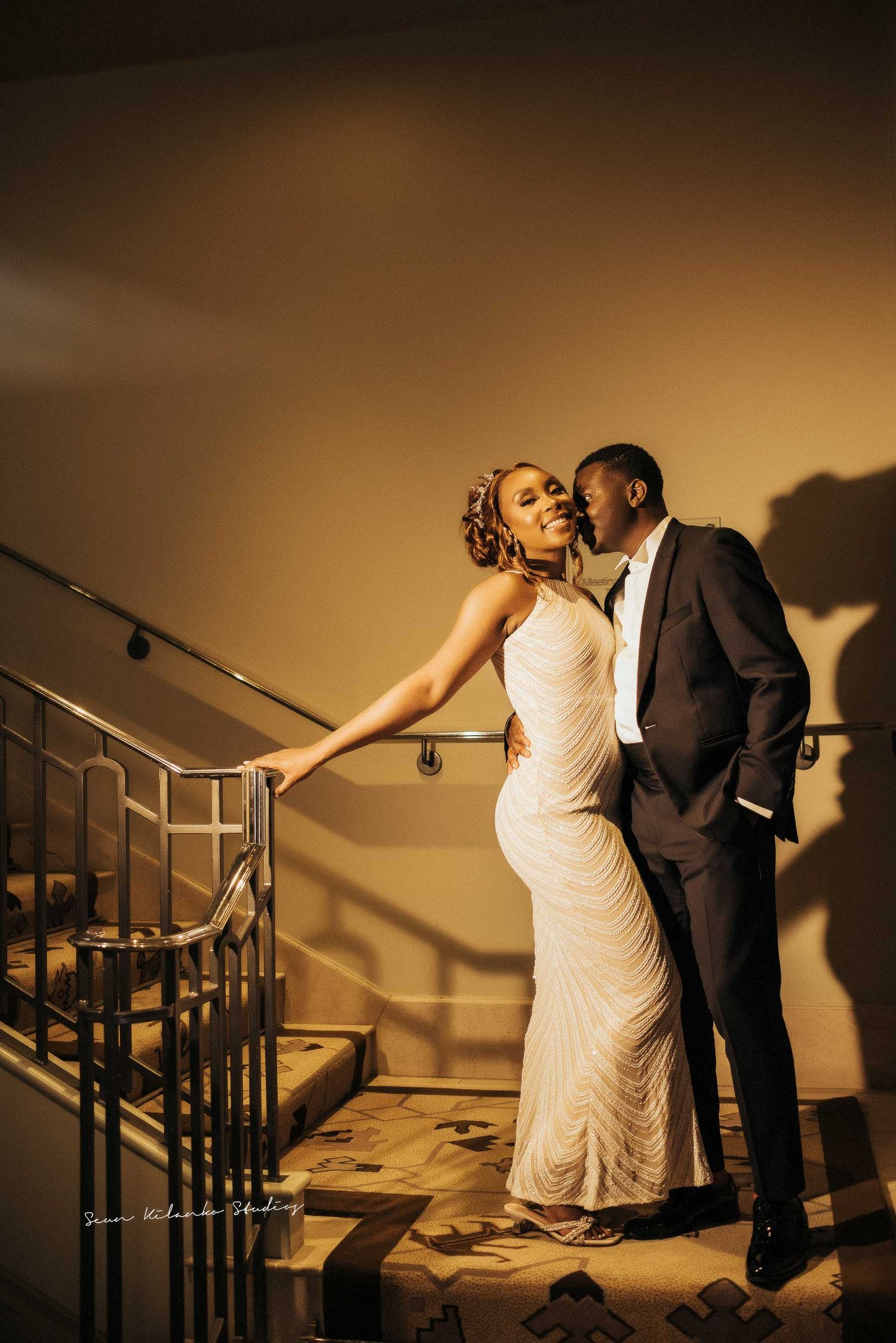 Romantic wedding couple poses on staircase with dramatic lighting and shadows.