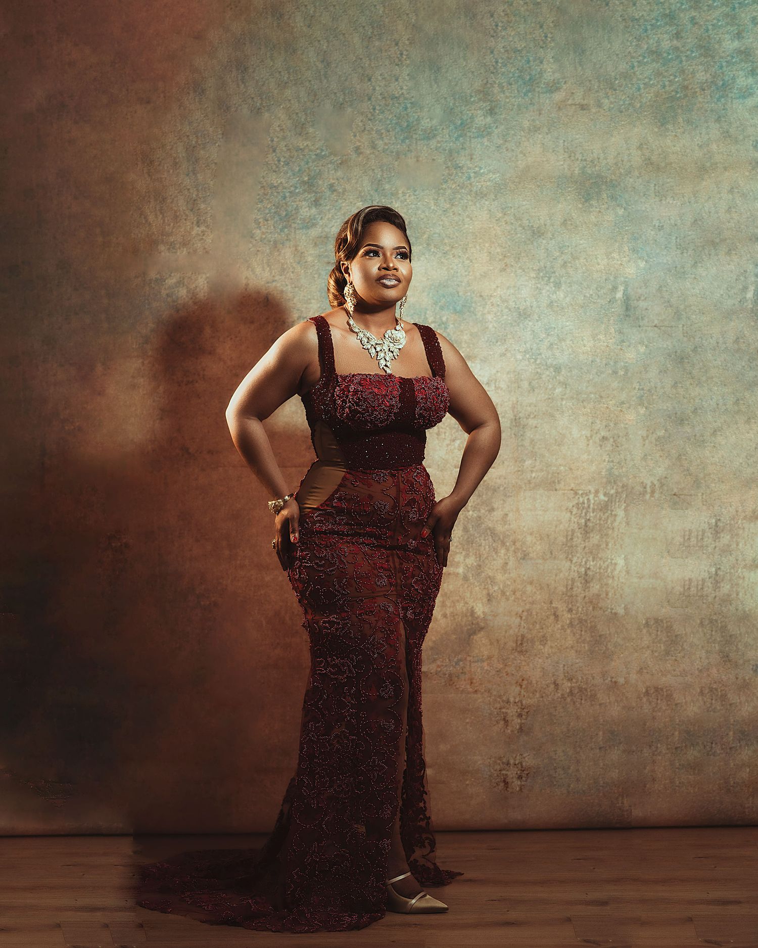 Confident pose in a burgundy mermaid dress with intricate lace details and statement jewelry.