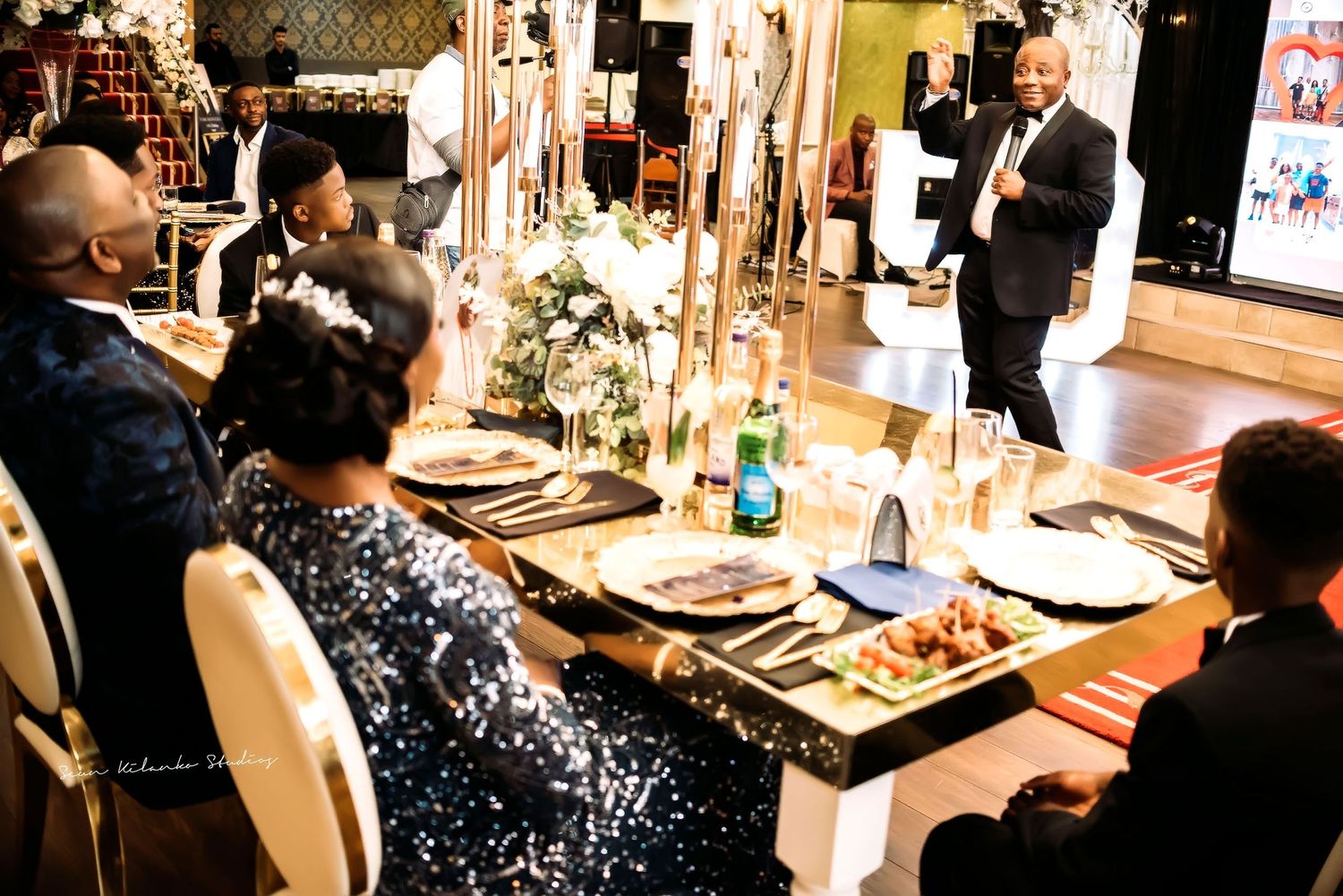 A speaker gives a presentation during an elegant dinner event with tall candle centerpieces and formal place settings.