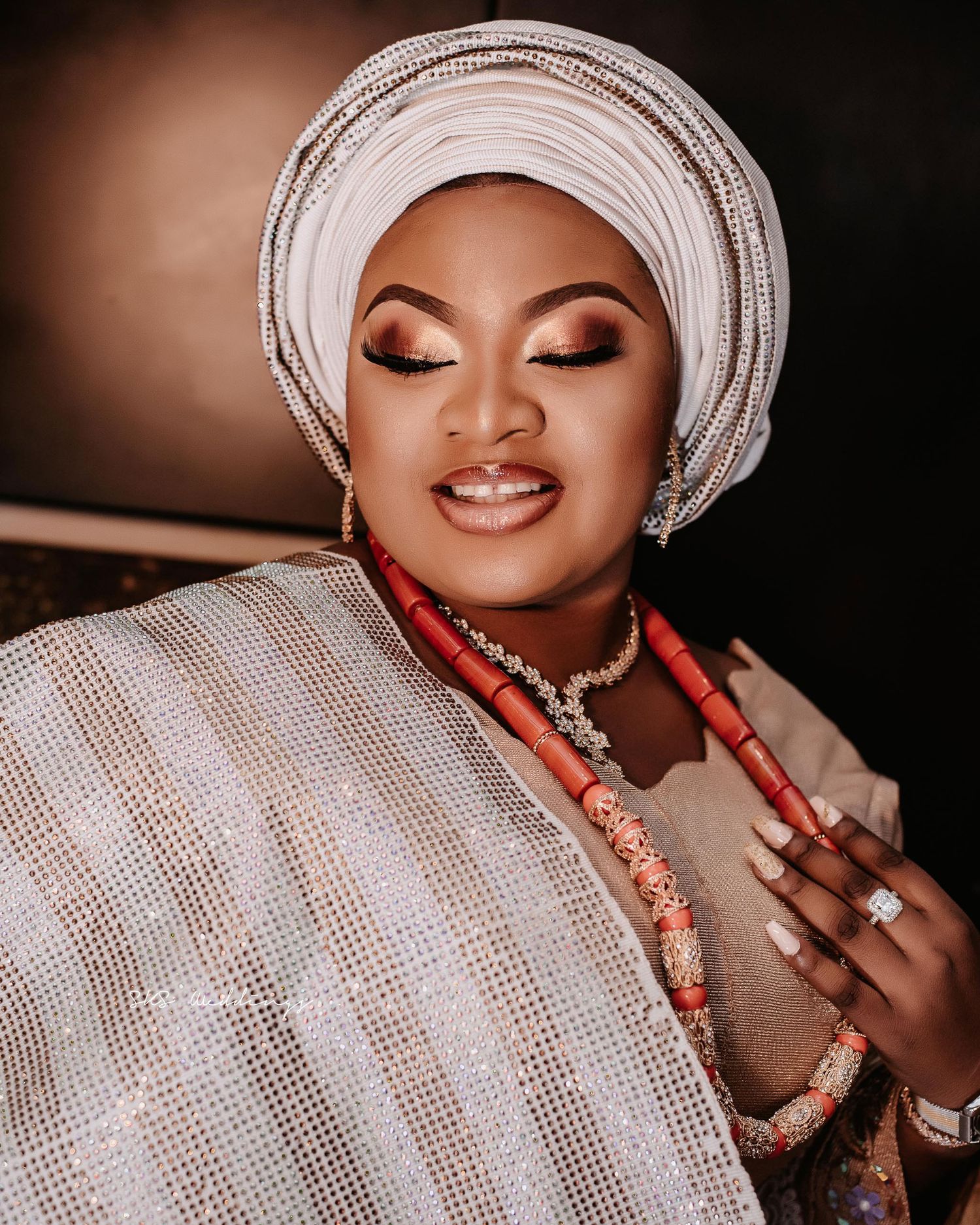 Close-up portrait of traditional African bride wearing white gele headwrap, coral beads and elegant makeup.