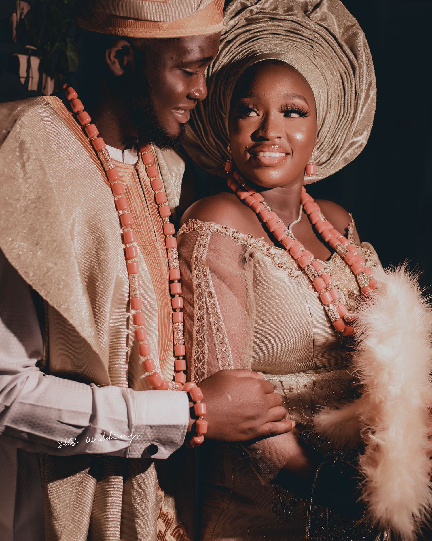 A couple in traditional Nigerian wedding attire with coral beads and gele headwear share an intimate moment together.