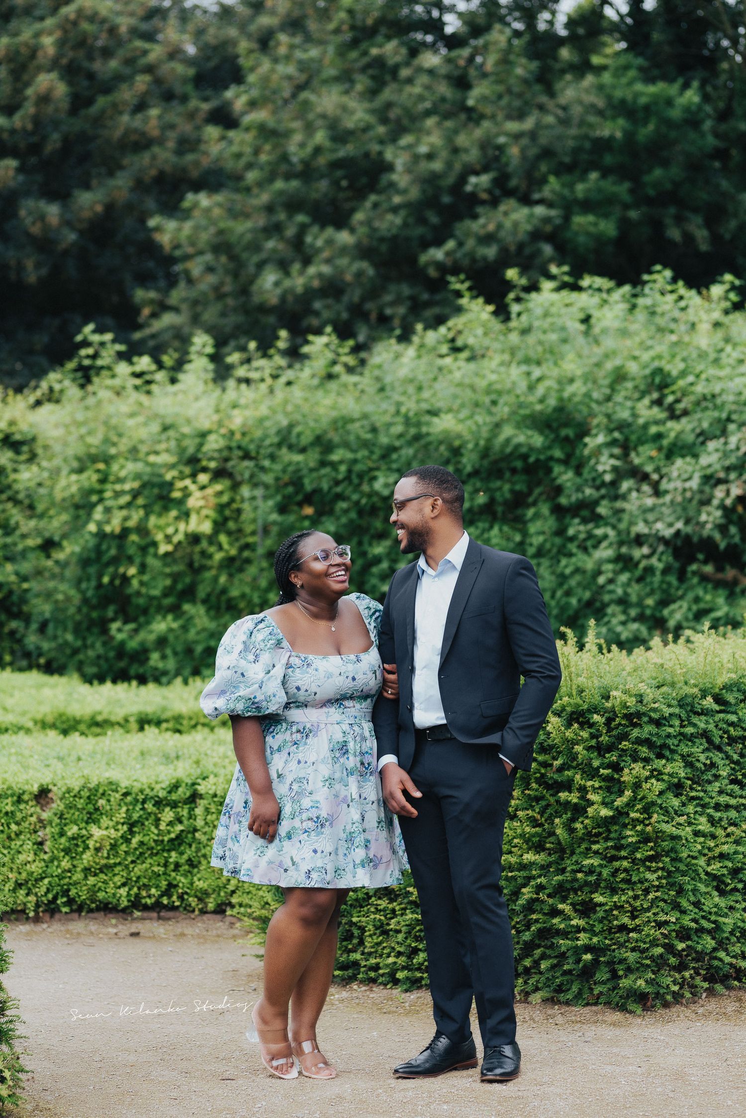 Couple shares a loving moment on garden path surrounded by manicured hedges.