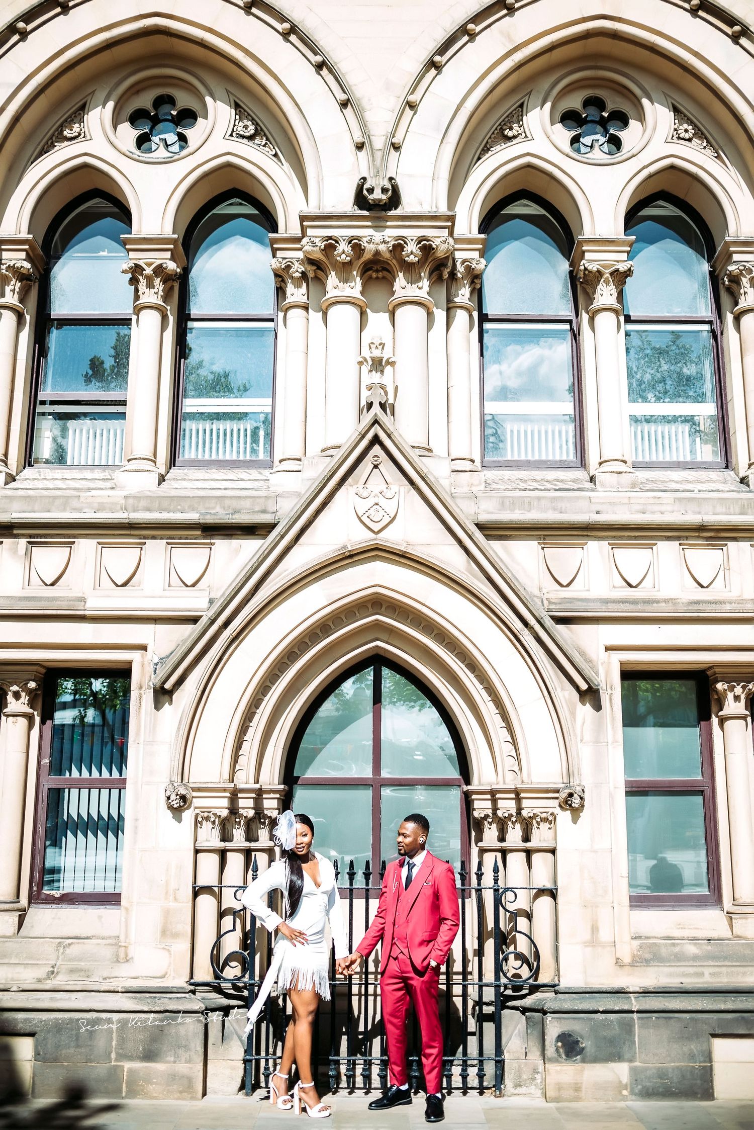Two people stand at entrance of historic Gothic architecture building with detailed stonework.