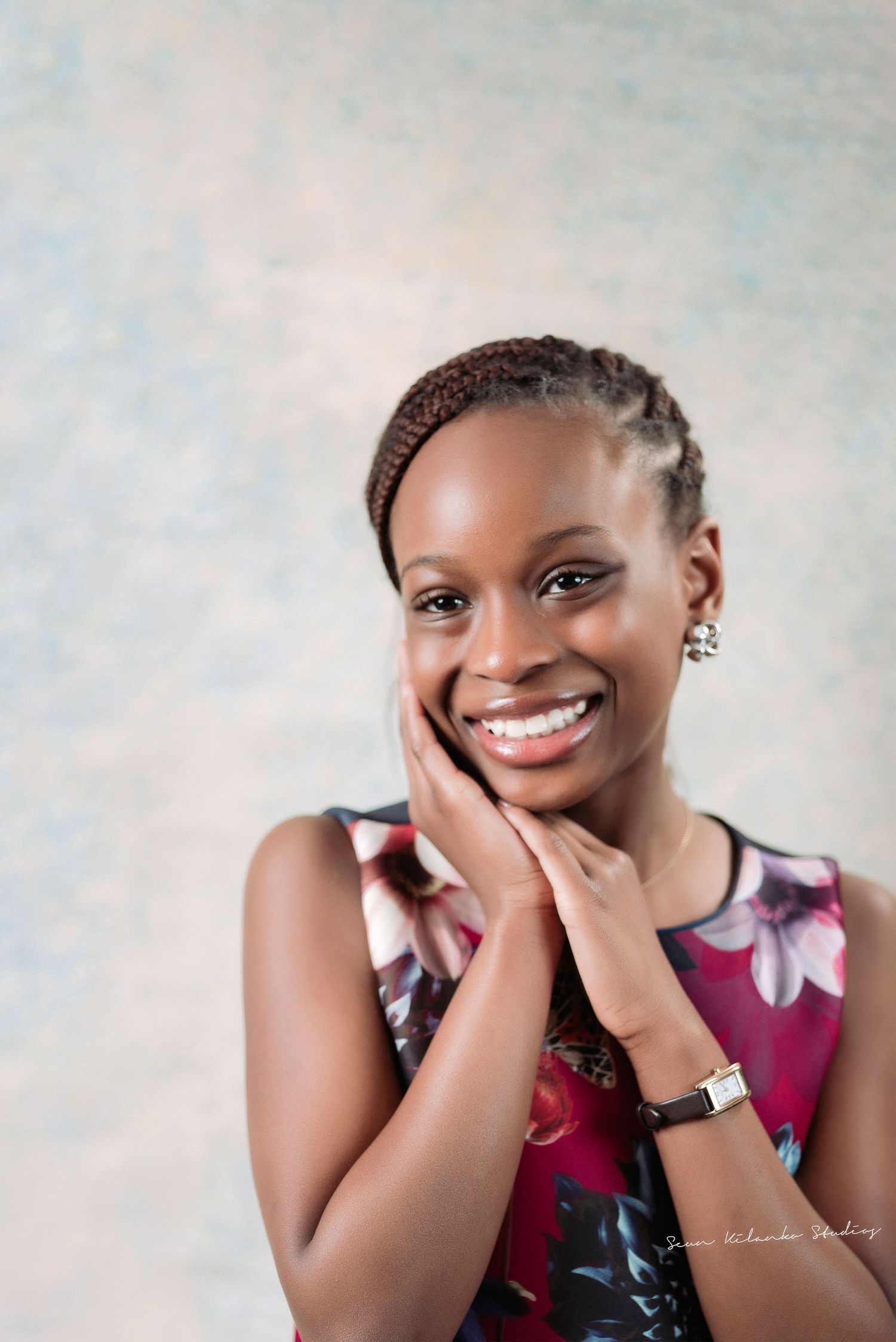 Close-up portrait showcasing braided hairstyle and warm smile against soft background.