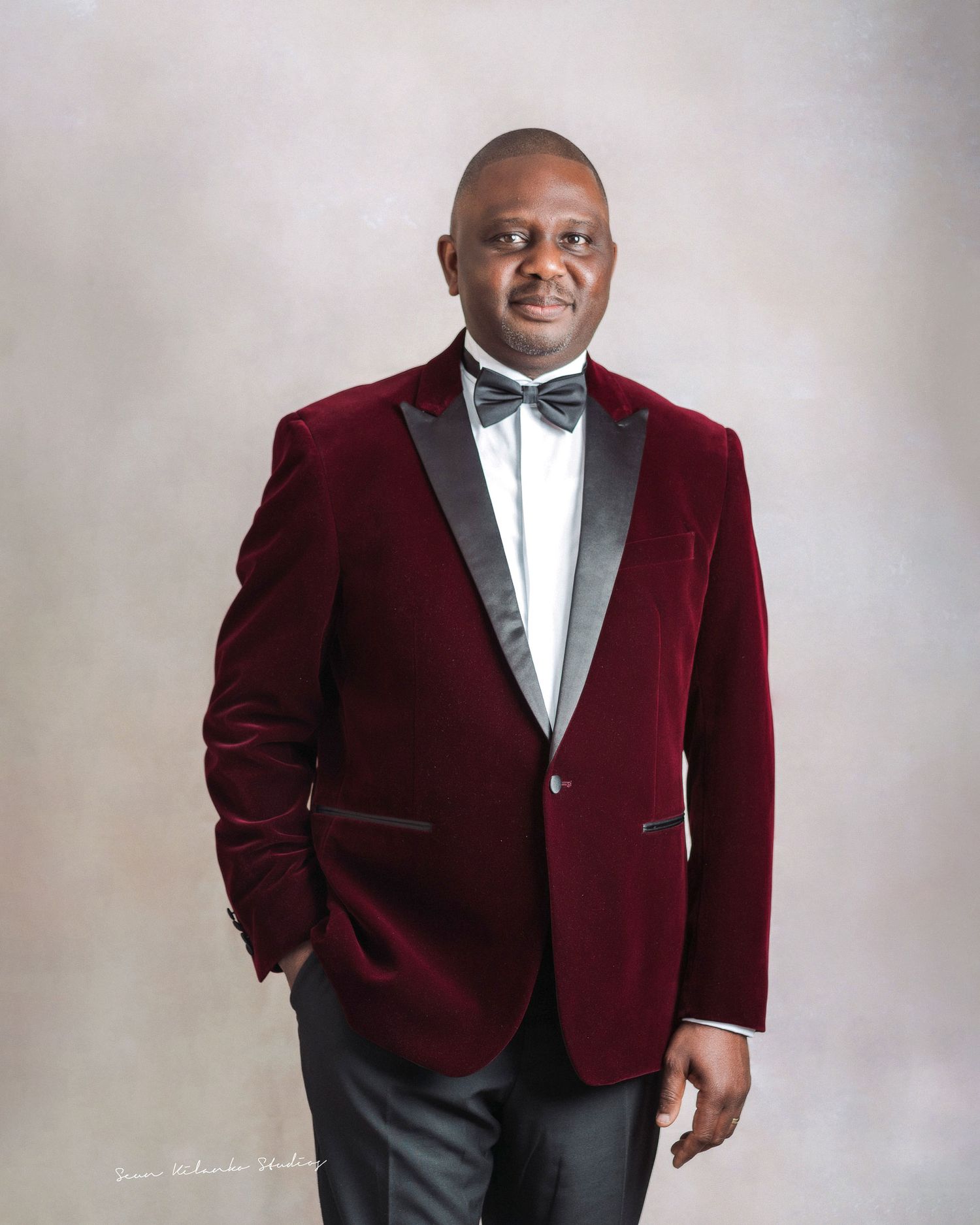 Formal portrait featuring someone in a burgundy velvet tuxedo jacket and bow tie.