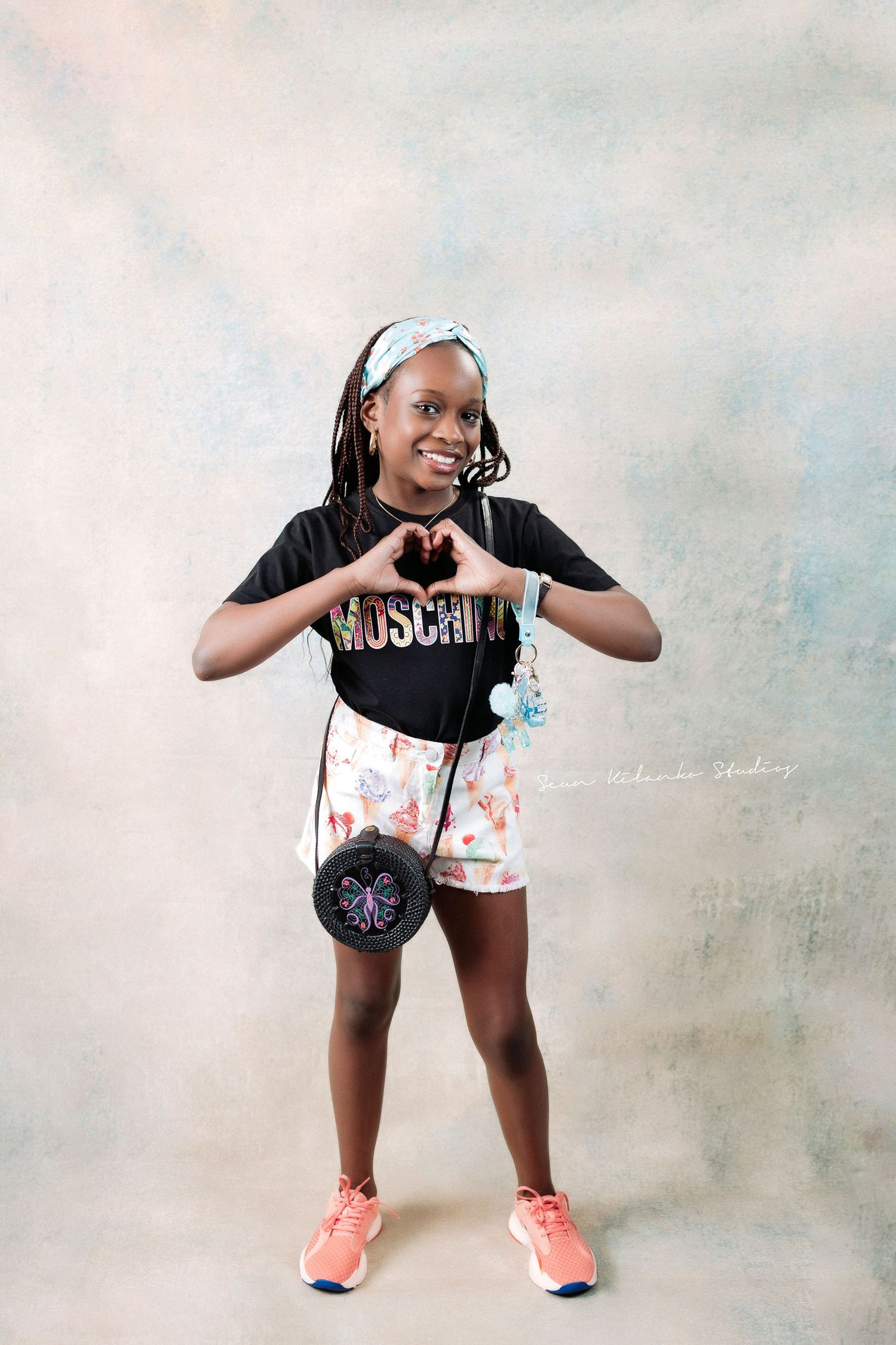 Playful pose making heart shape with hands while wearing Moschino shirt and floral shorts.
