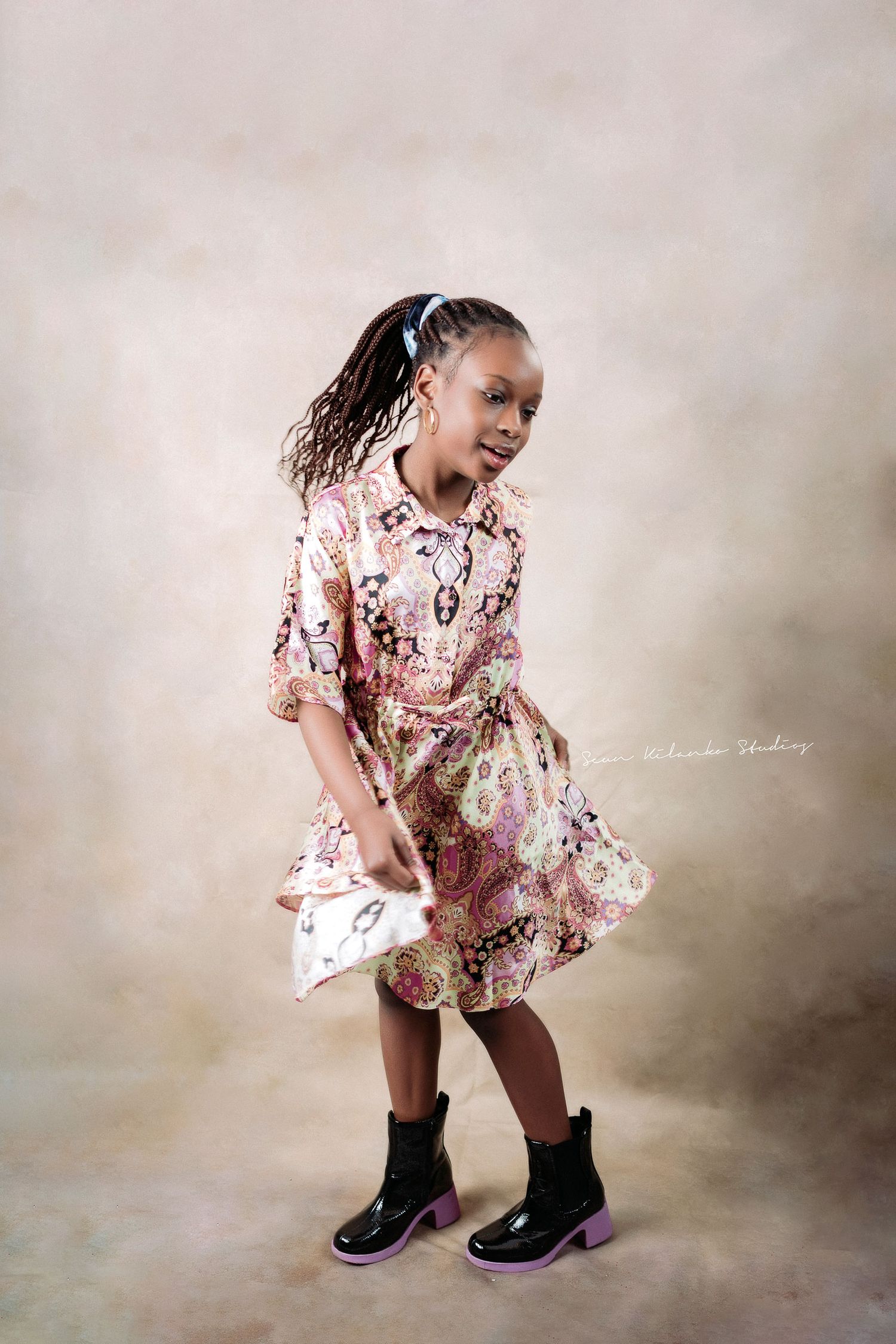Young dancer in floral dress and boots twirling joyfully against neutral backdrop.