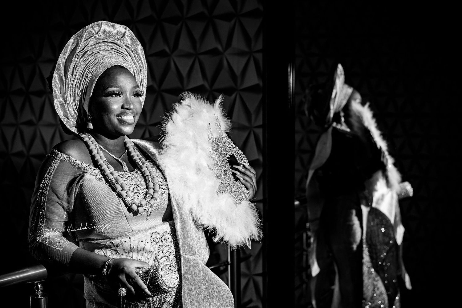 A performer in traditional African attire holds a white feather fan on stage during a black and white performance.