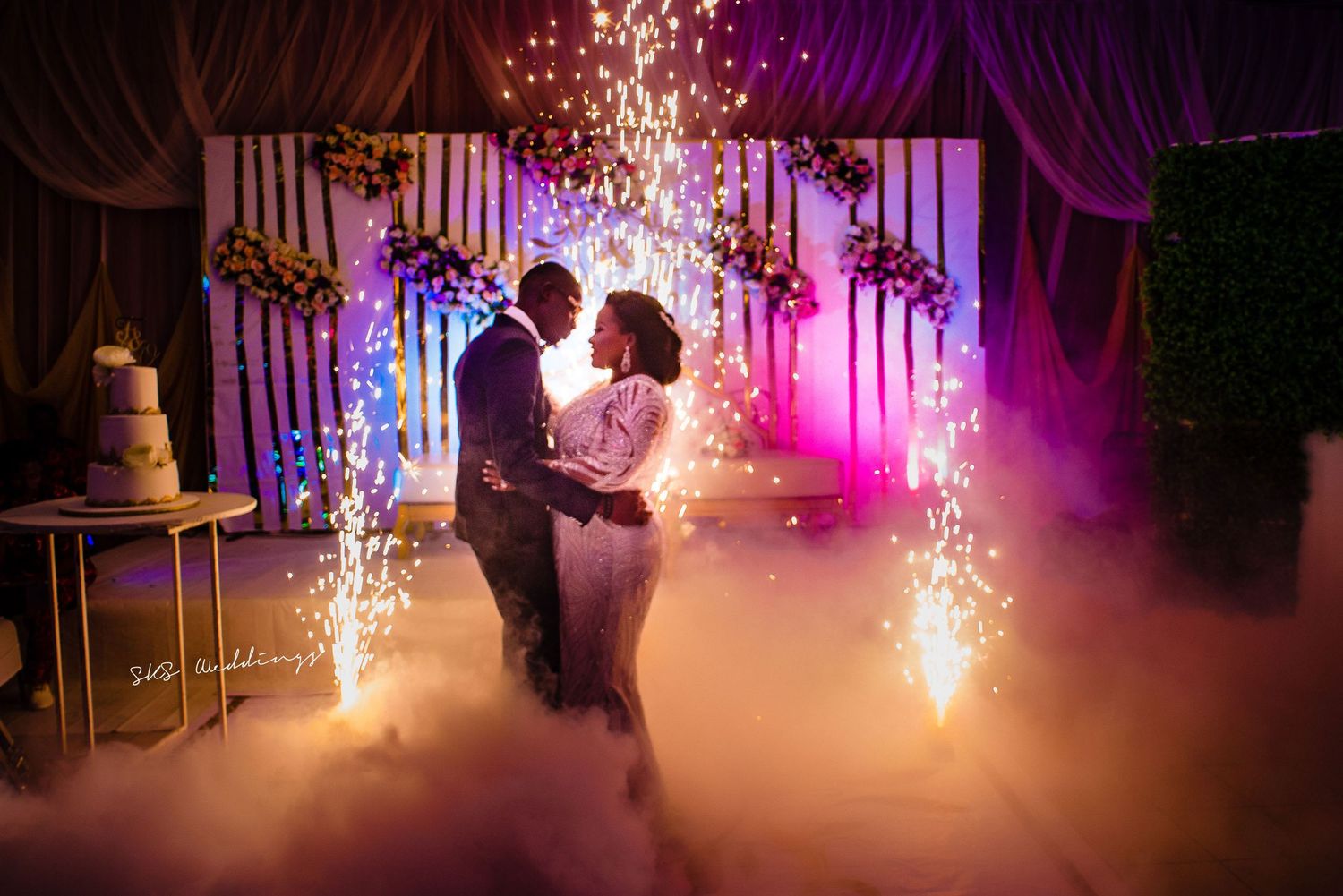 A couple shares their first dance at their wedding reception surrounded by sparklers and purple lighting effects.
