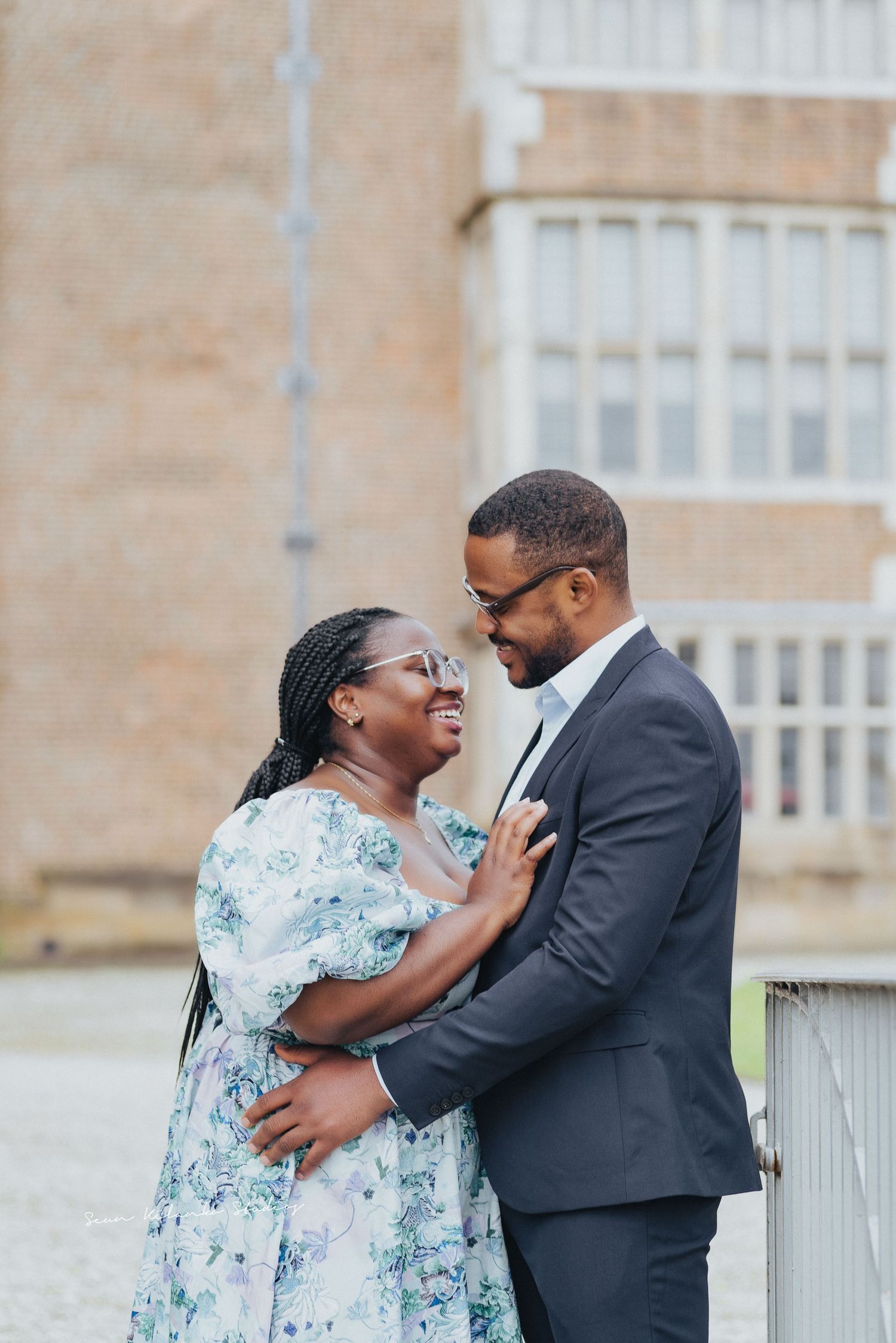 Romantic couple embraces tenderly in front of stone building wearing formal attire.
