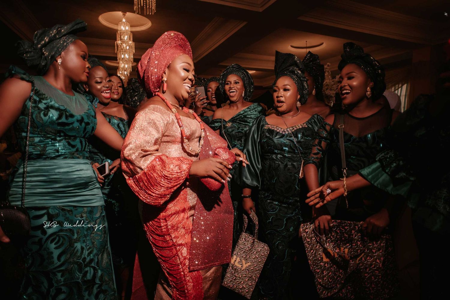 A group of women in elegant formal attire laughing together at a celebration event with warm lighting.