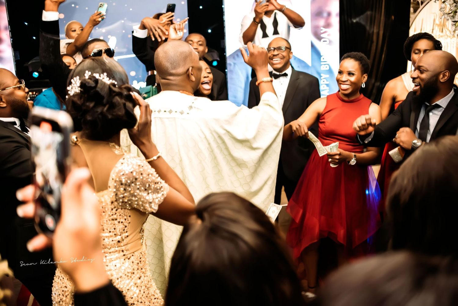 A lively crowd dances and celebrates at an elegant party with shimmering decor and festive atmosphere.