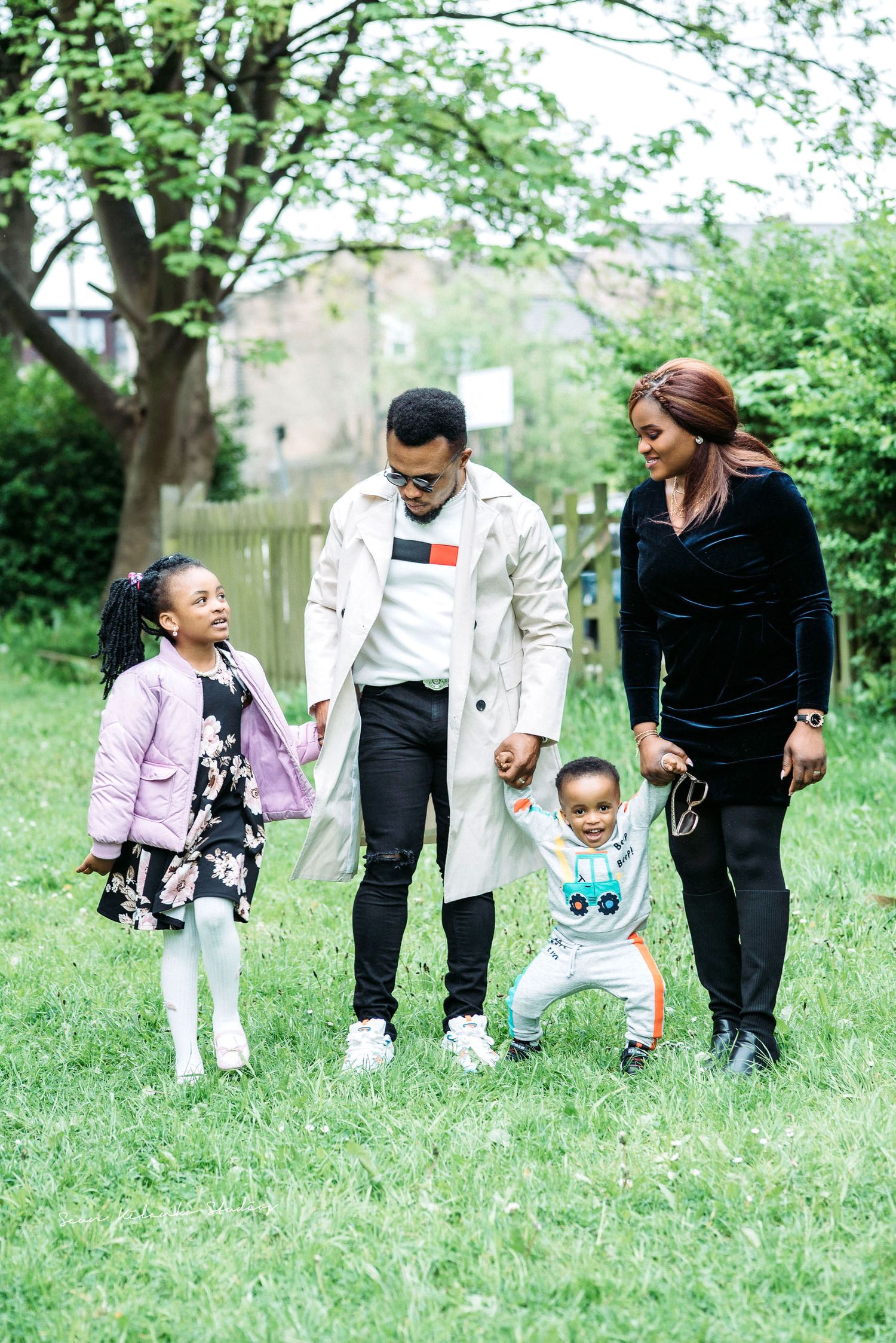 A family walks together and smiles while enjoying a spring day in a lush green park setting.