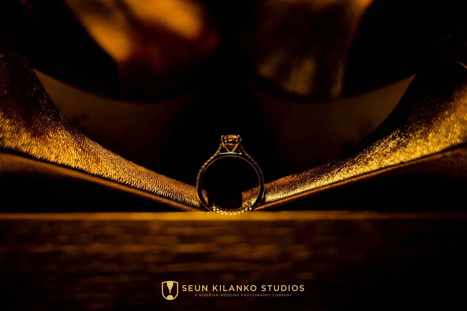 Wedding ring macro photography shot through pages of book creating dramatic golden lighting effect.
