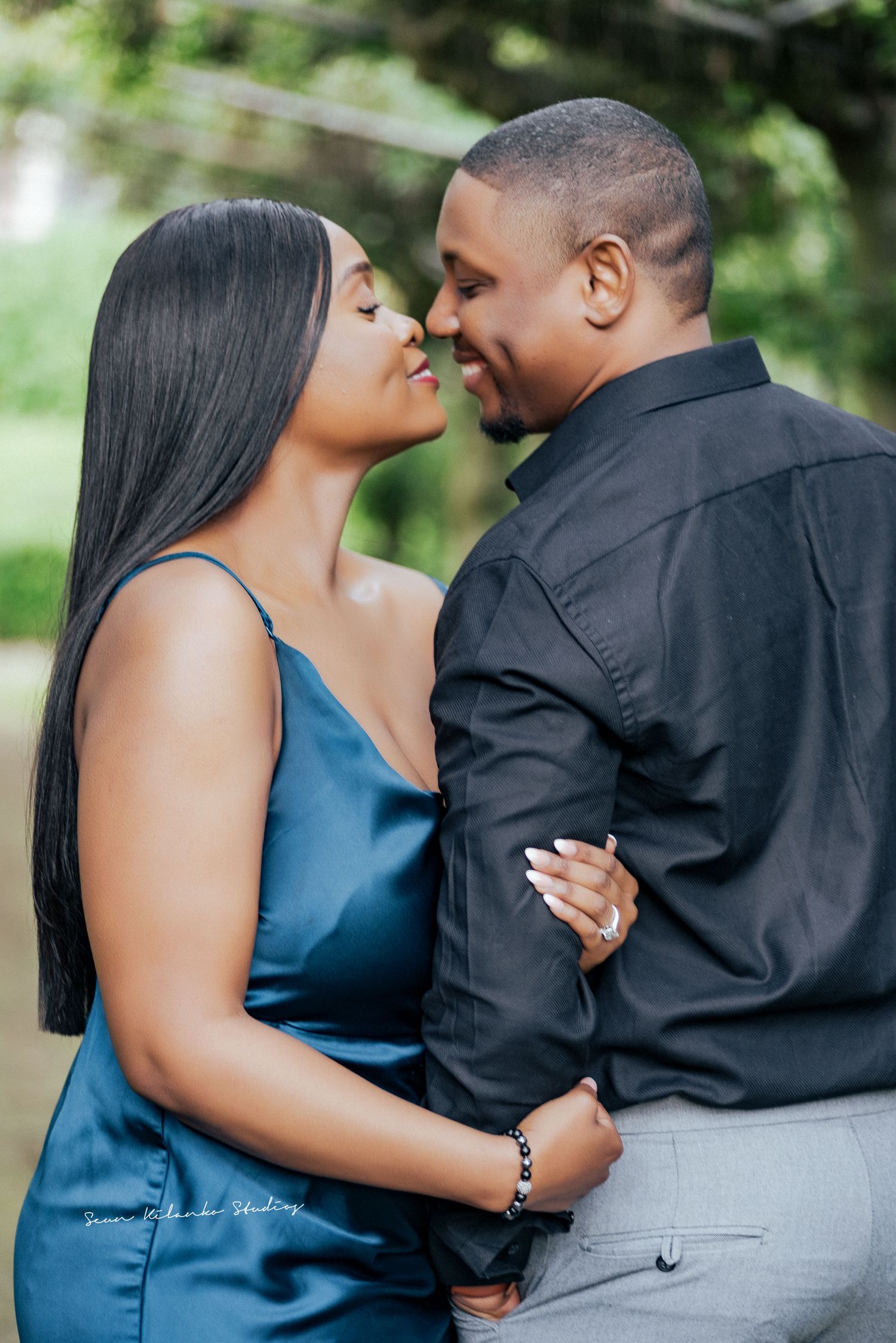 A couple shares an intimate moment in a garden setting wearing coordinated blue and black outfits.