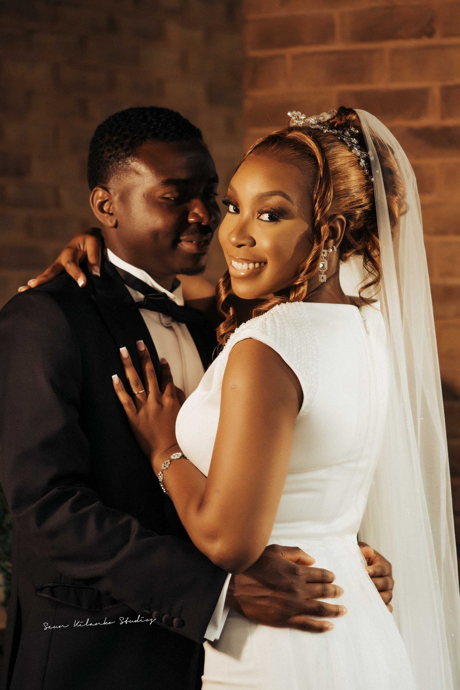 An intimate wedding portrait showing a tender embrace against a brick wall background.