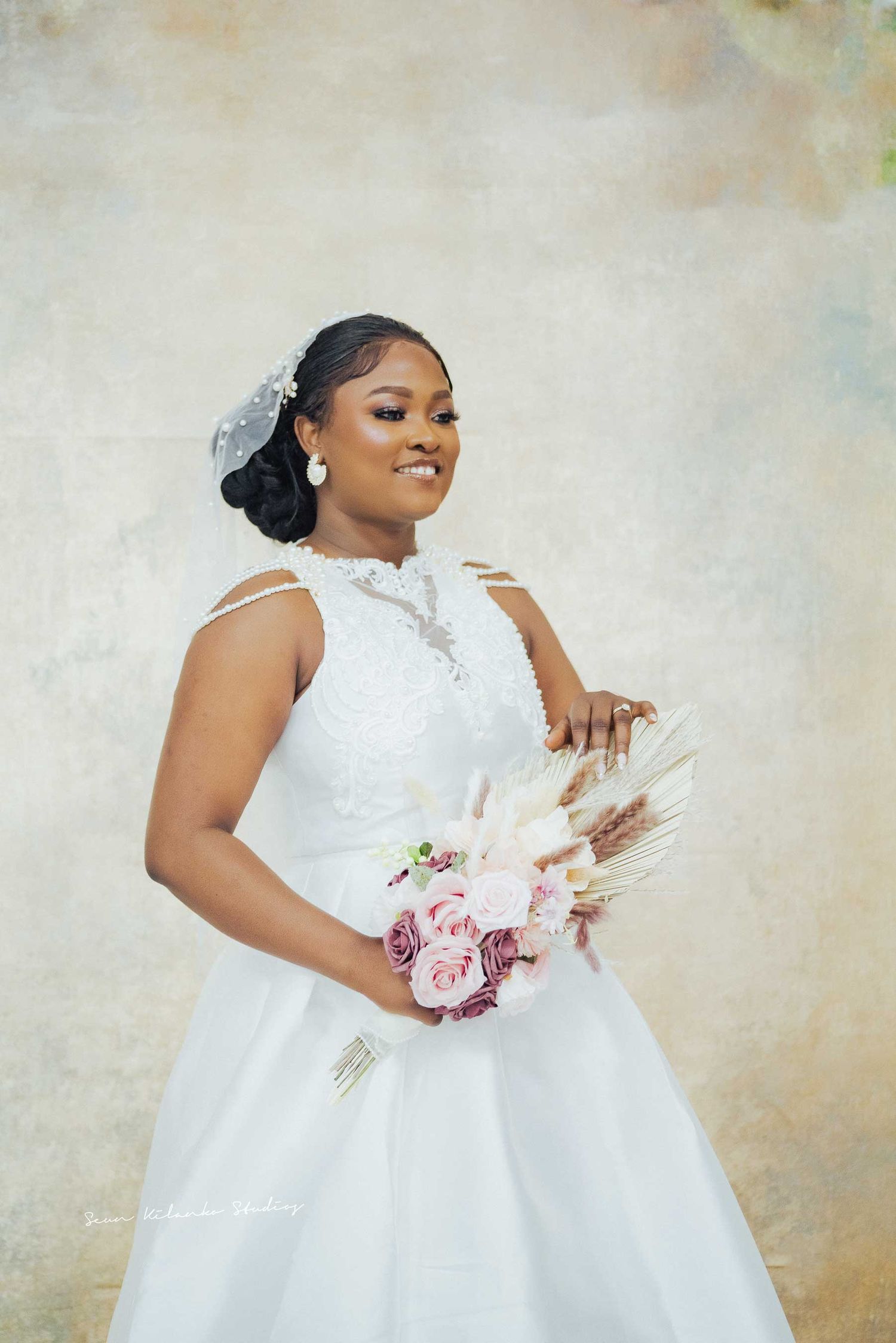 Elegant bride holds floral bouquet while wearing detailed white wedding gown.