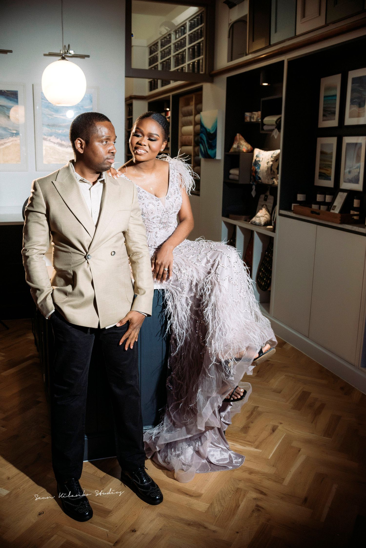 Stylish couple poses in chic indoor setting with bride in detailed lace gown.