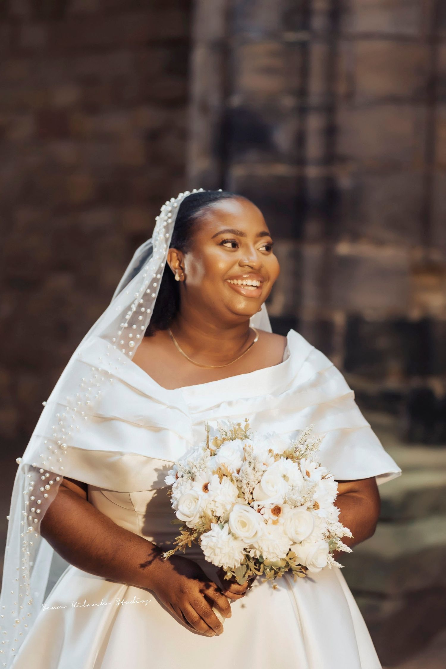 Radiant bride in white gown holds beautiful bouquet of white flowers.